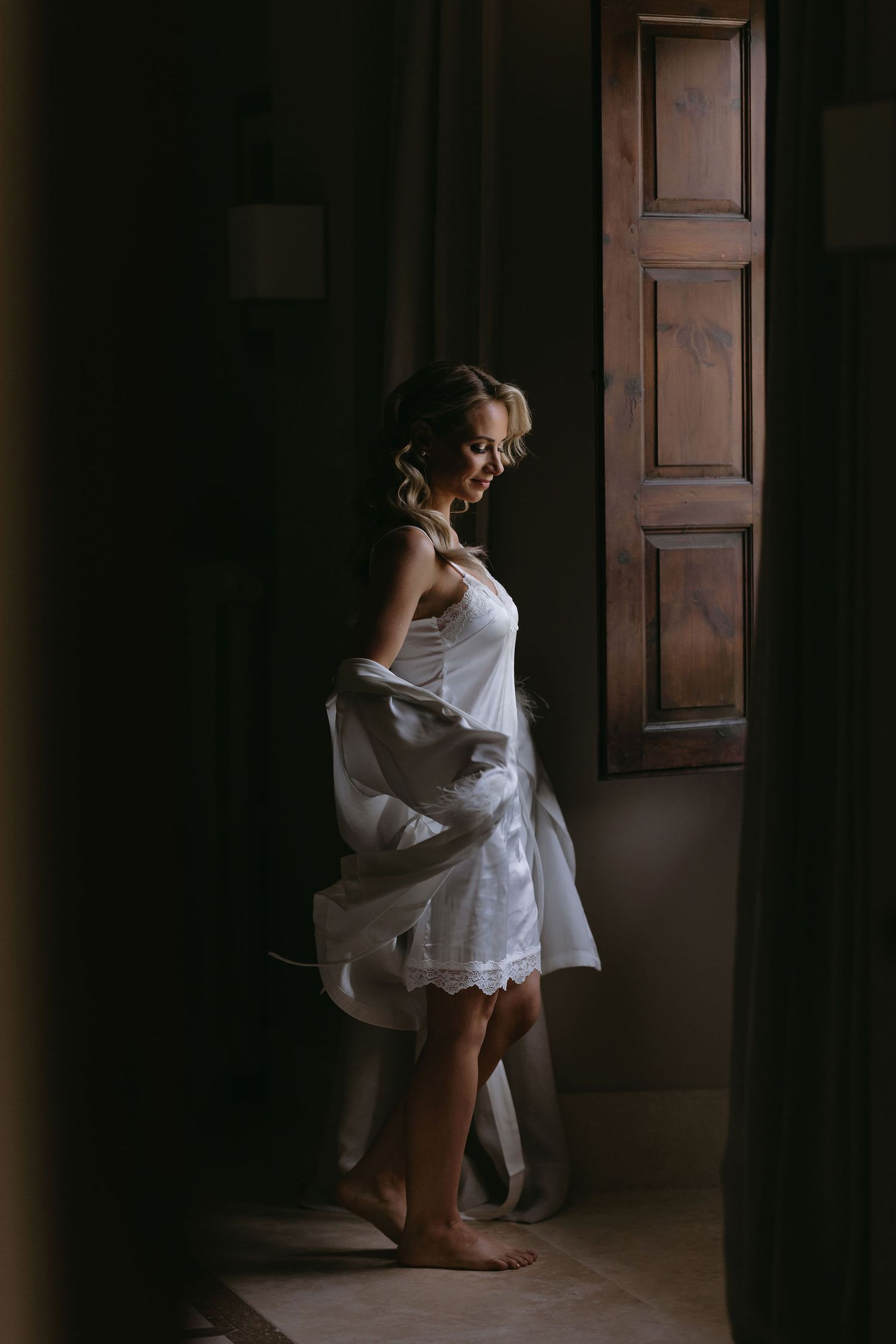 Artistic silhouette photo of a person in white dress standing by a wooden window.