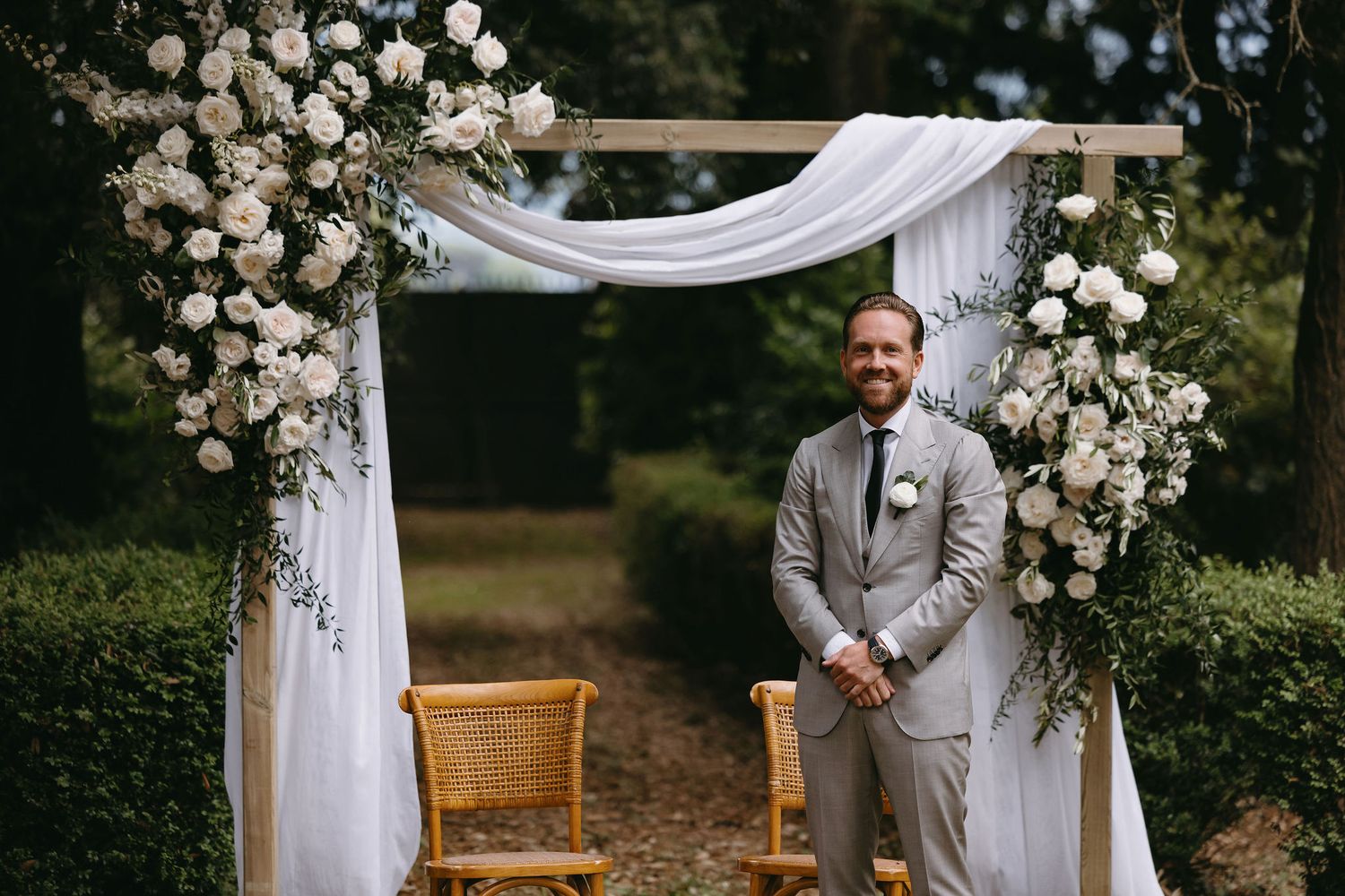 Wedding arch decorated with white roses and flowing fabric in an outdoor garden setting.
