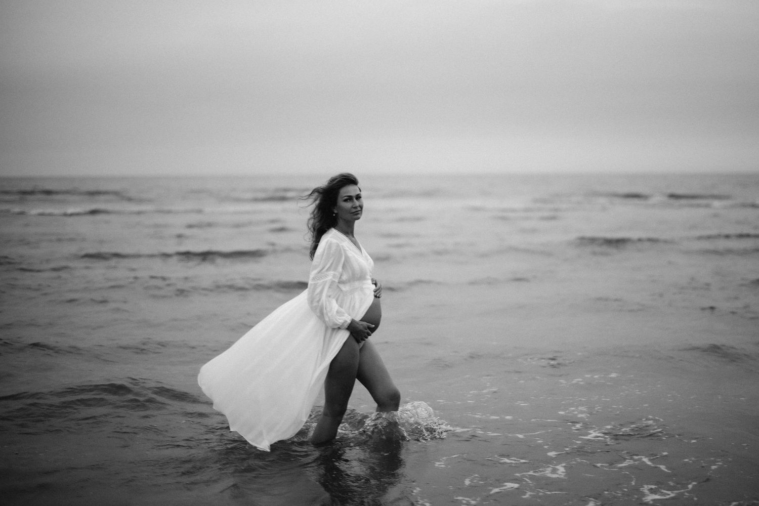 Black and white series of photos showing a person in a flowing white dress walking into ocean waves.