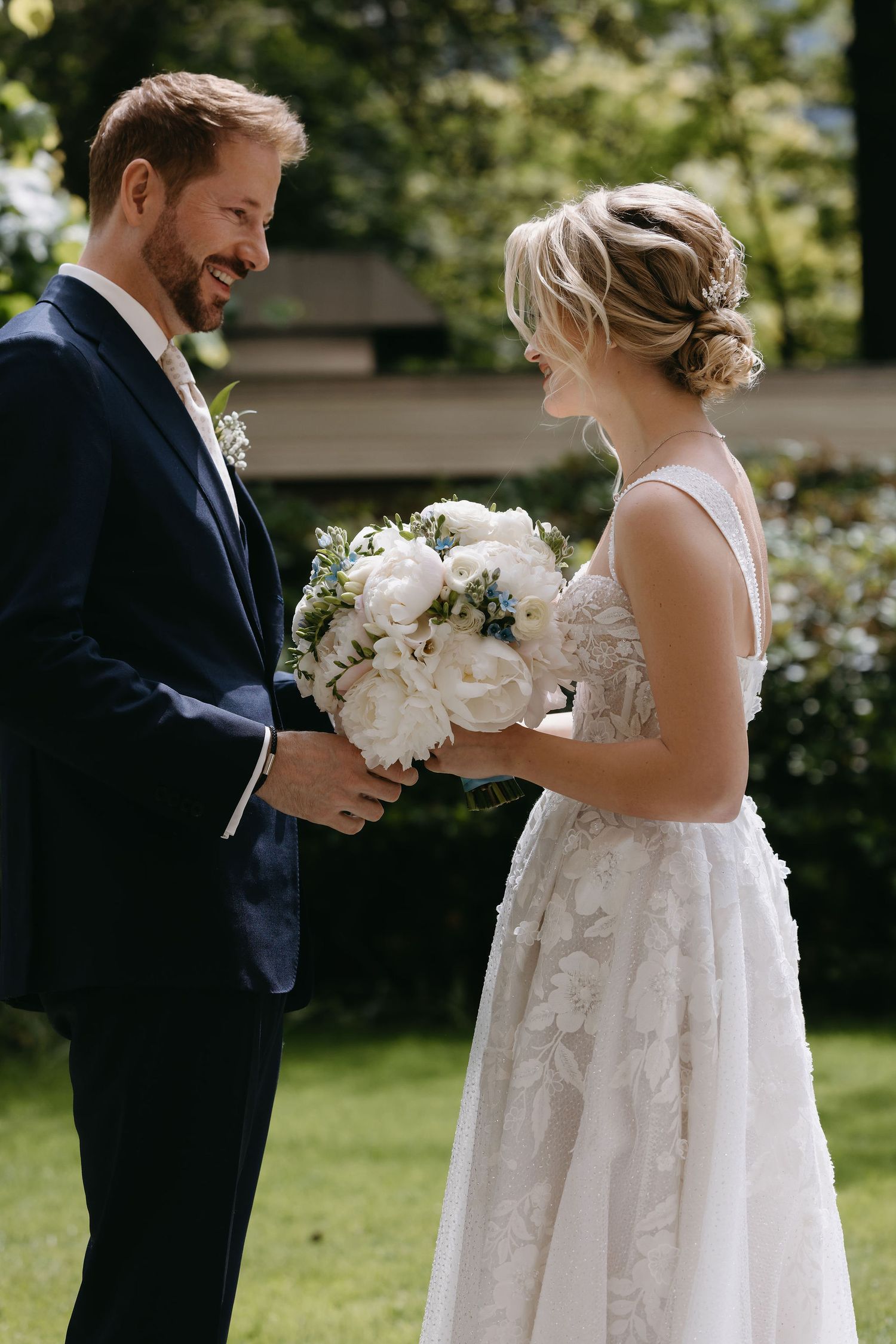 A white bridal bouquet with delicate peonies and roses being exchanged during an outdoor garden ceremony.