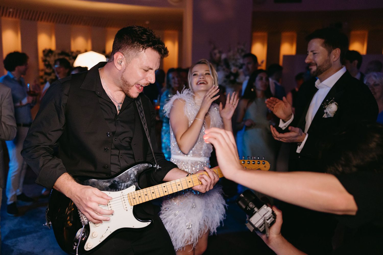 Wedding band performs energetically at reception with musician playing guitar and guests dancing on dance floor.