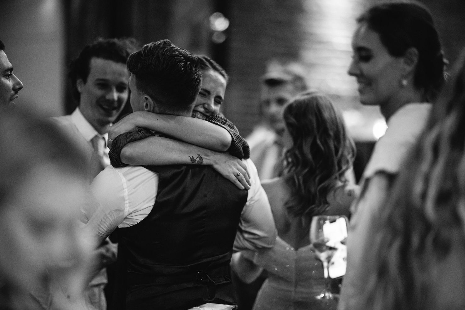 Wedding guests embrace and dance together during an emotional reception celebration.