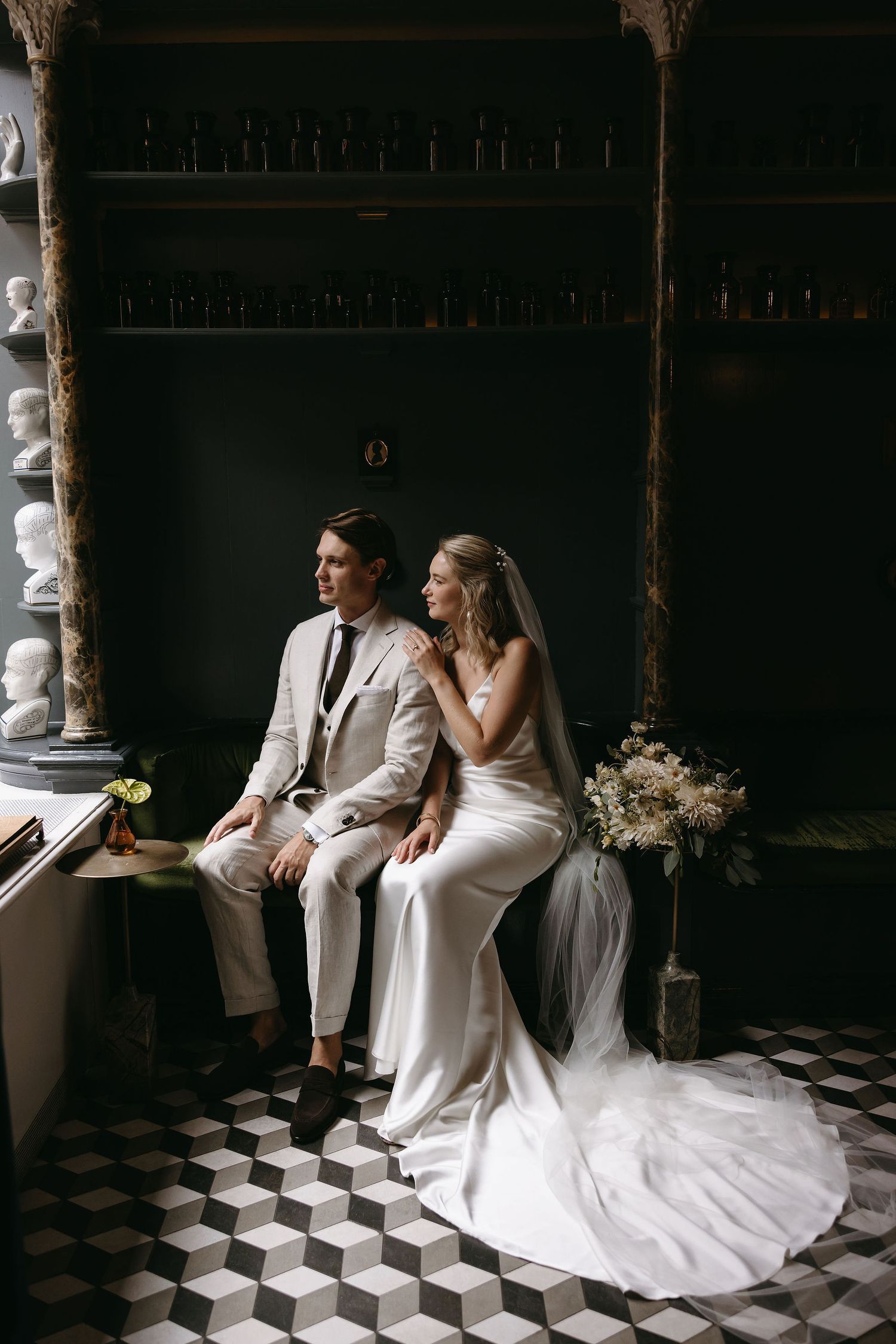 Wedding couple sitting on checkered floor against dark vintage bar backdrop.