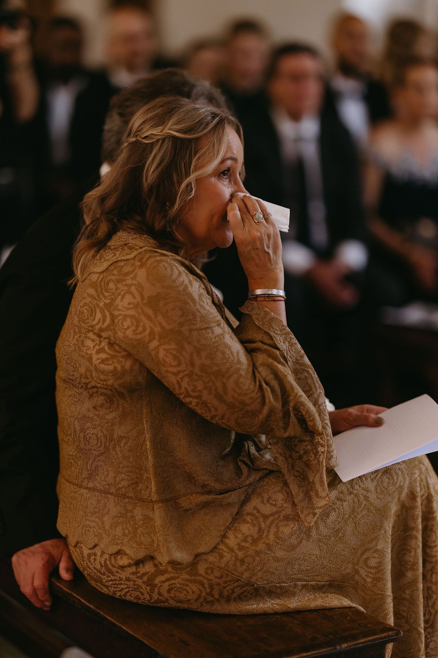An emotional guest in a lace dress wipes tears during a wedding ceremony.
