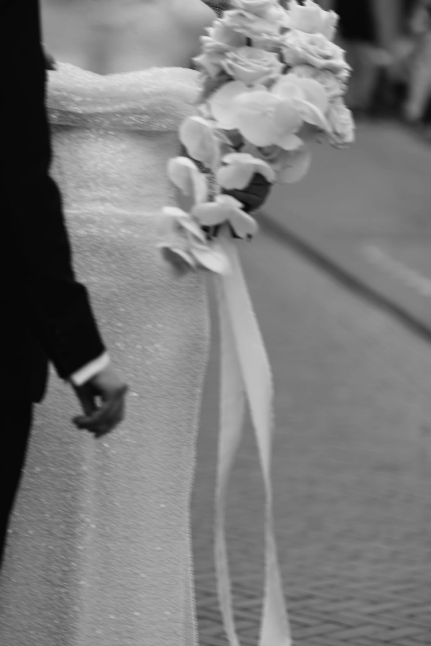 Close-up detail of white wedding dress with floral decorations and flowing ribbons.