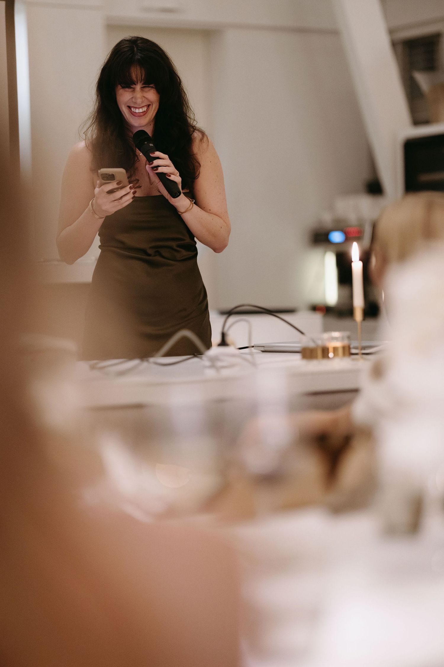 A speaker holds a microphone and phone during an indoor event speech or presentation.