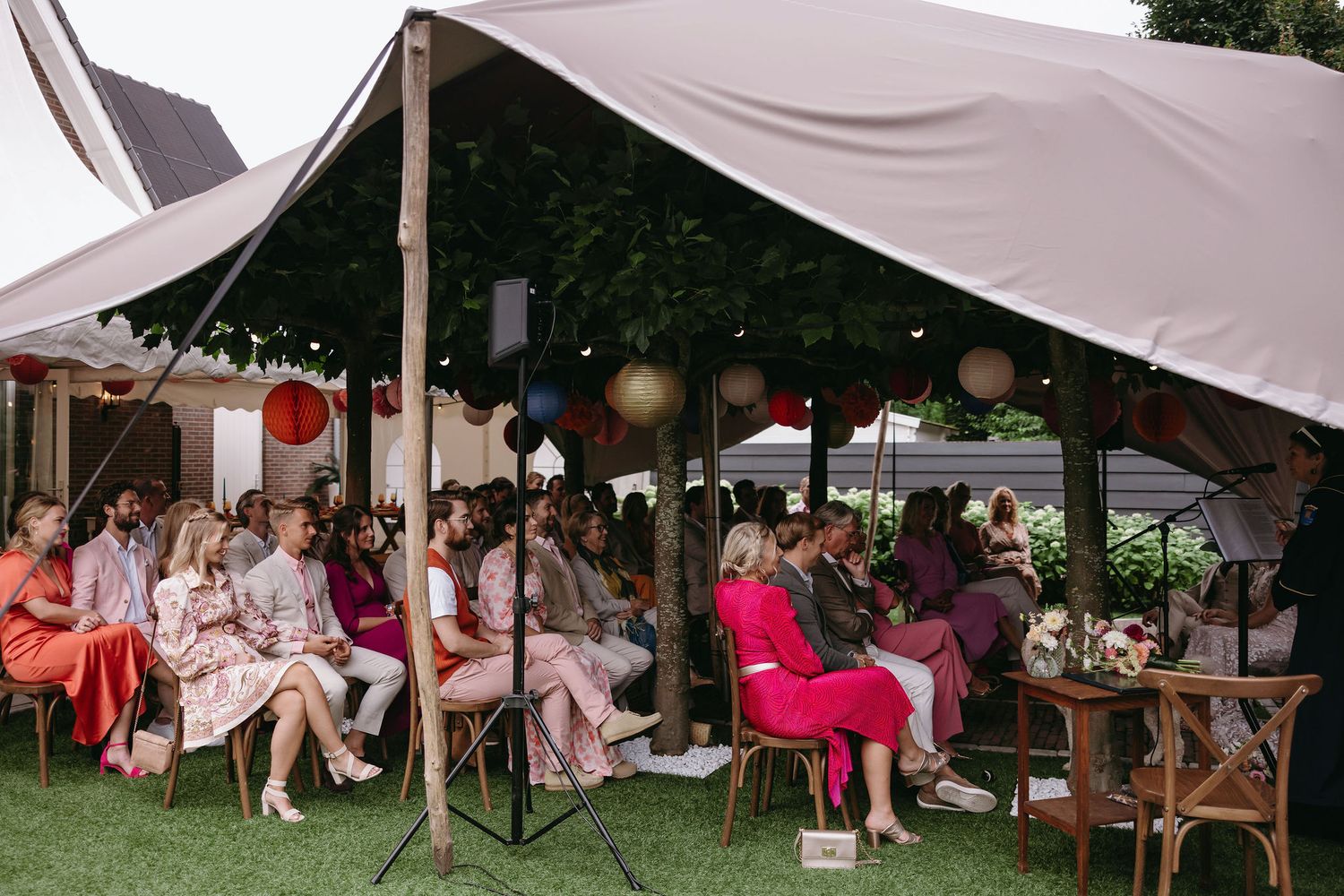 A white tent covers outdoor seating at a wedding reception with string lights creating ambiance.