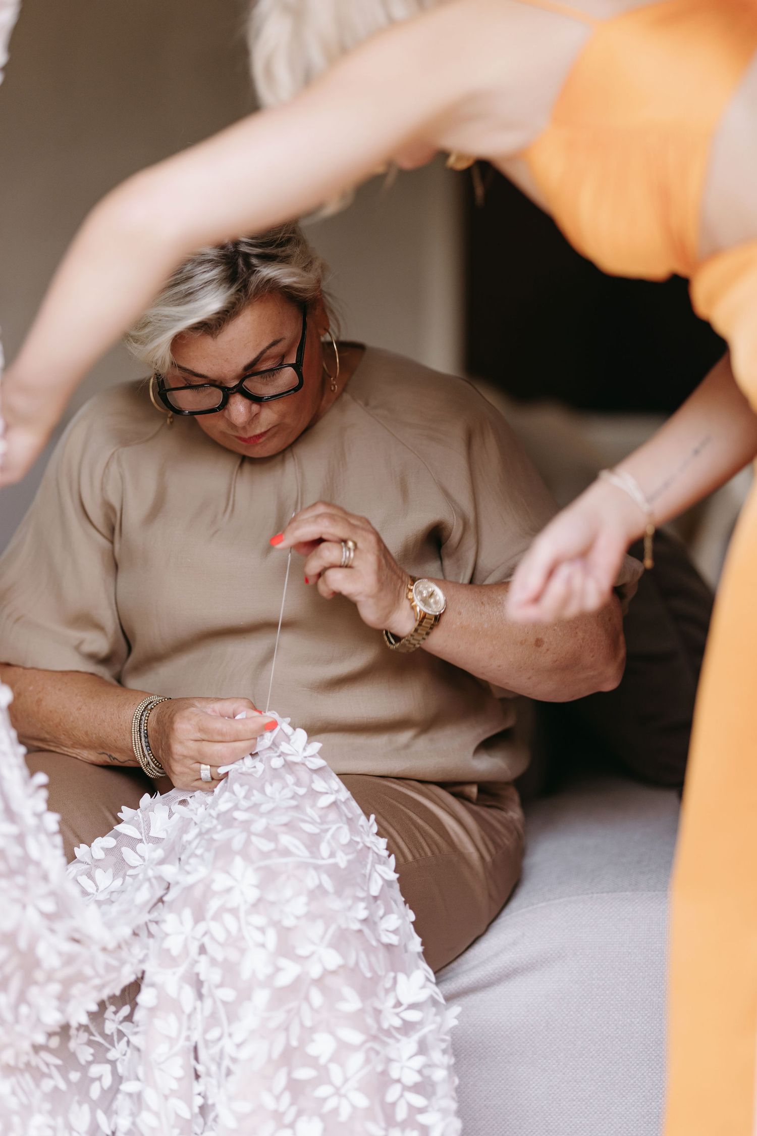 Close-up of hands working with delicate white fabric details during wedding preparations.