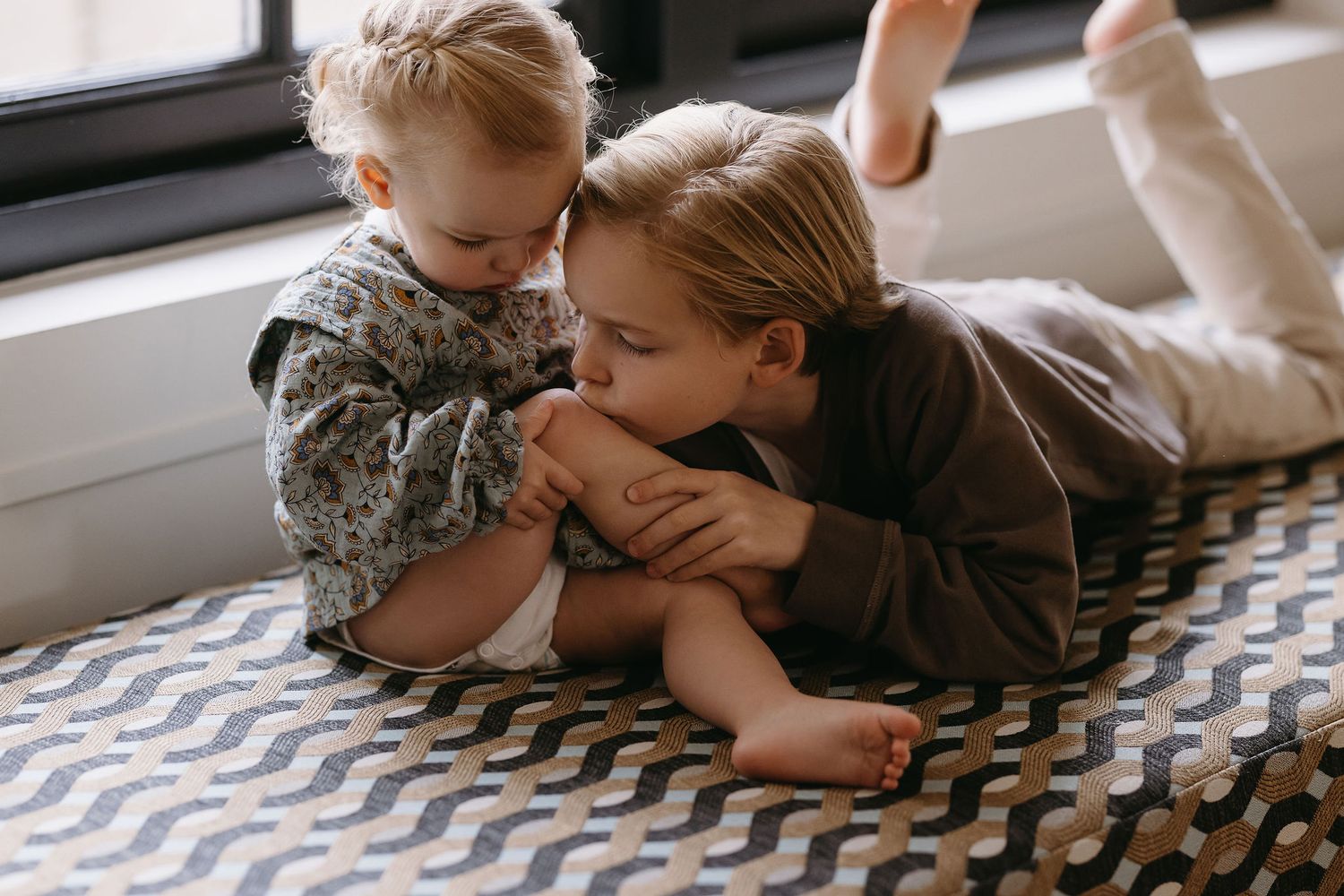 Intimate black and white portrait of children sharing sweet moment on chevron blanket.