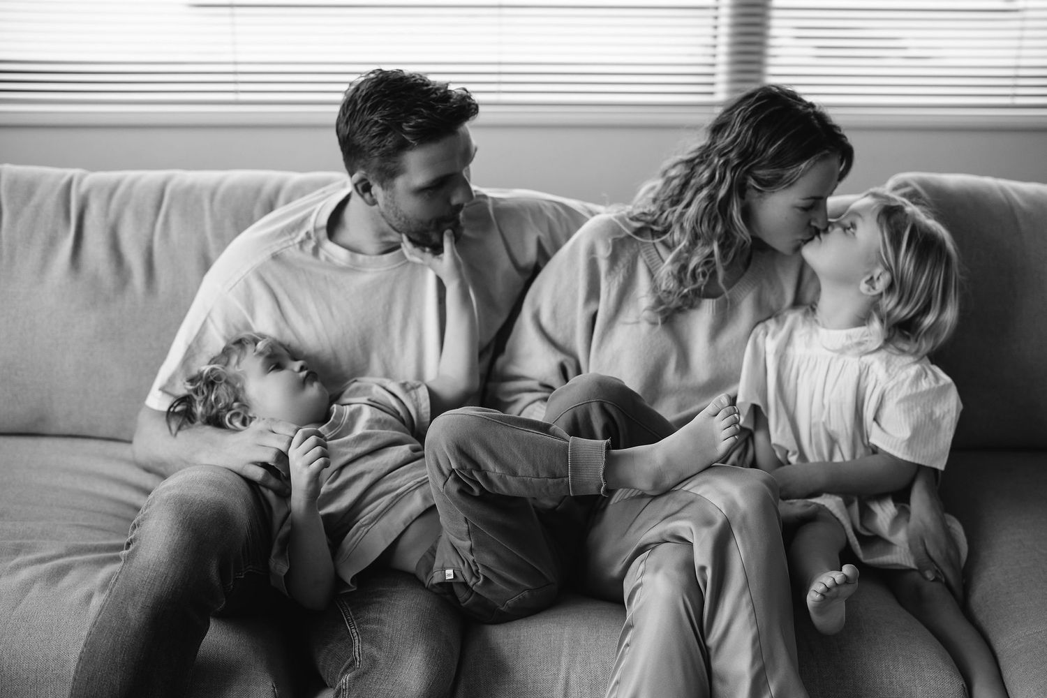 An intimate black and white portrait of a family sharing a tender moment on the couch.