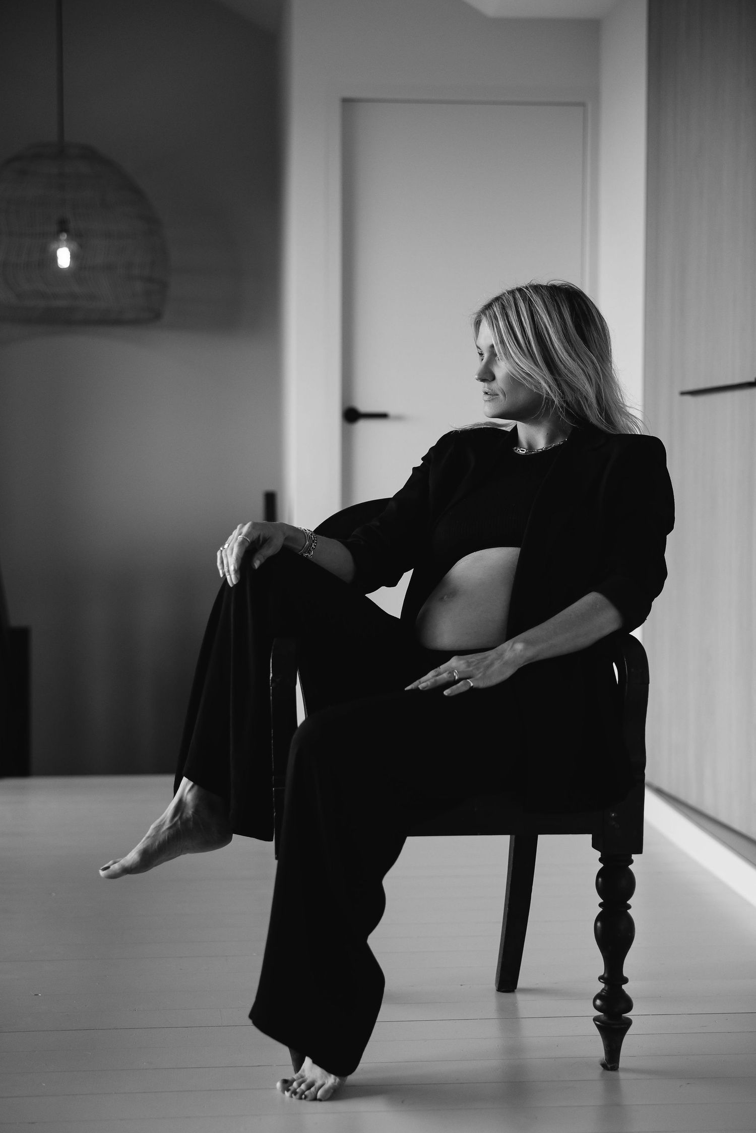 Black and white portrait of pregnant woman relaxing in elegant chair by window.