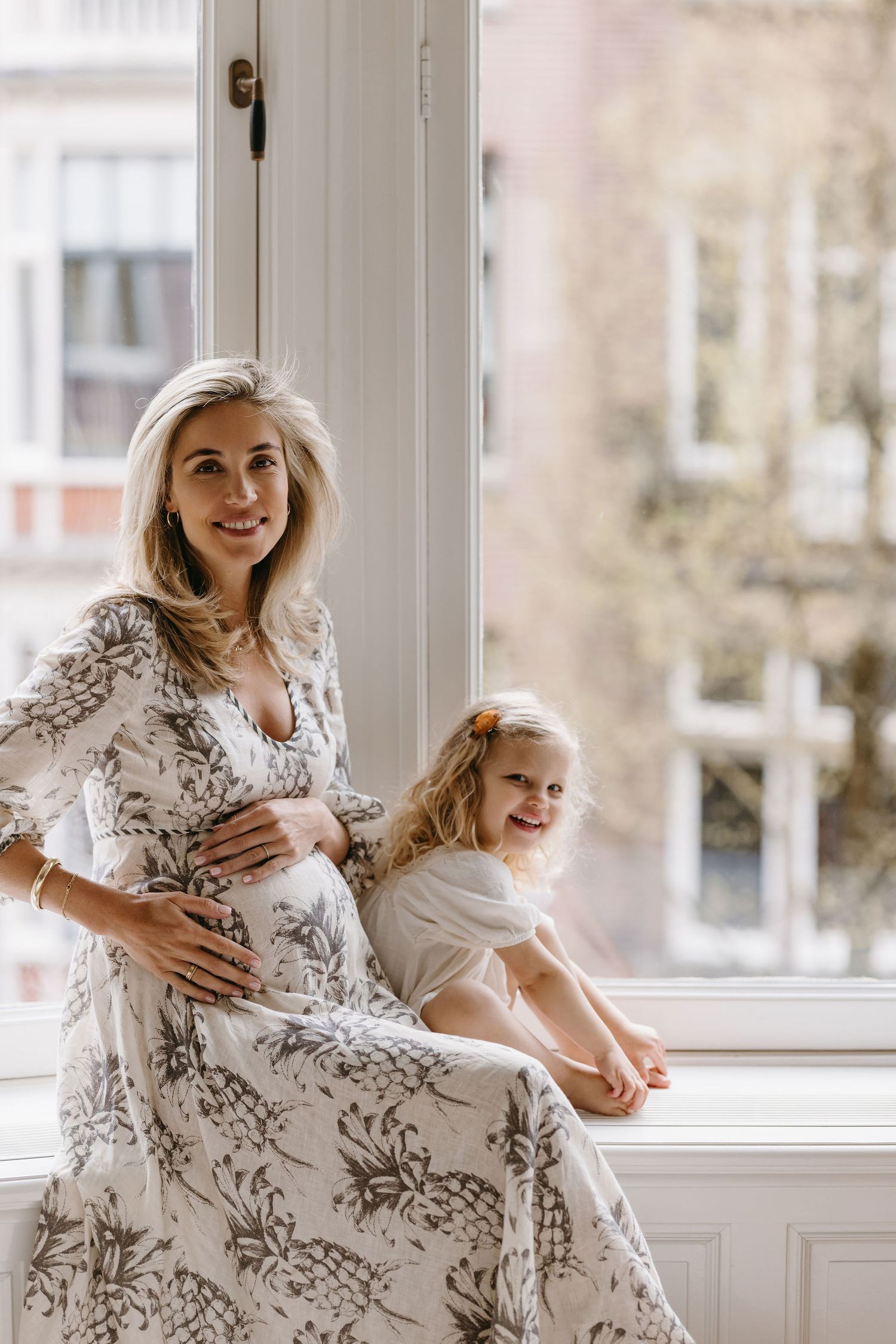Mother and child share tender moments by a window in floral dress during lifestyle photoshoot.