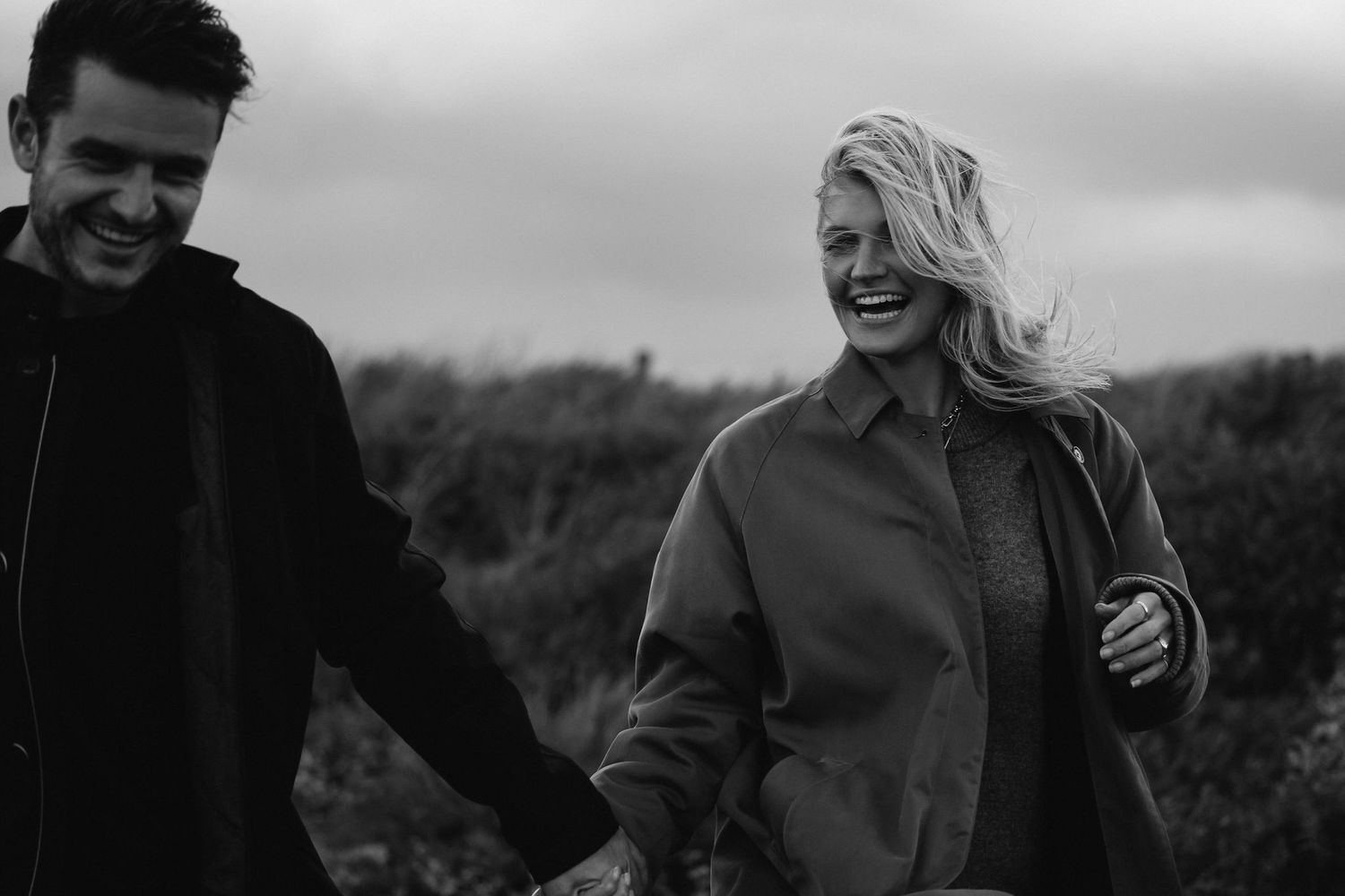 Black and white outdoor photo of embracing couple against rural backdrop.