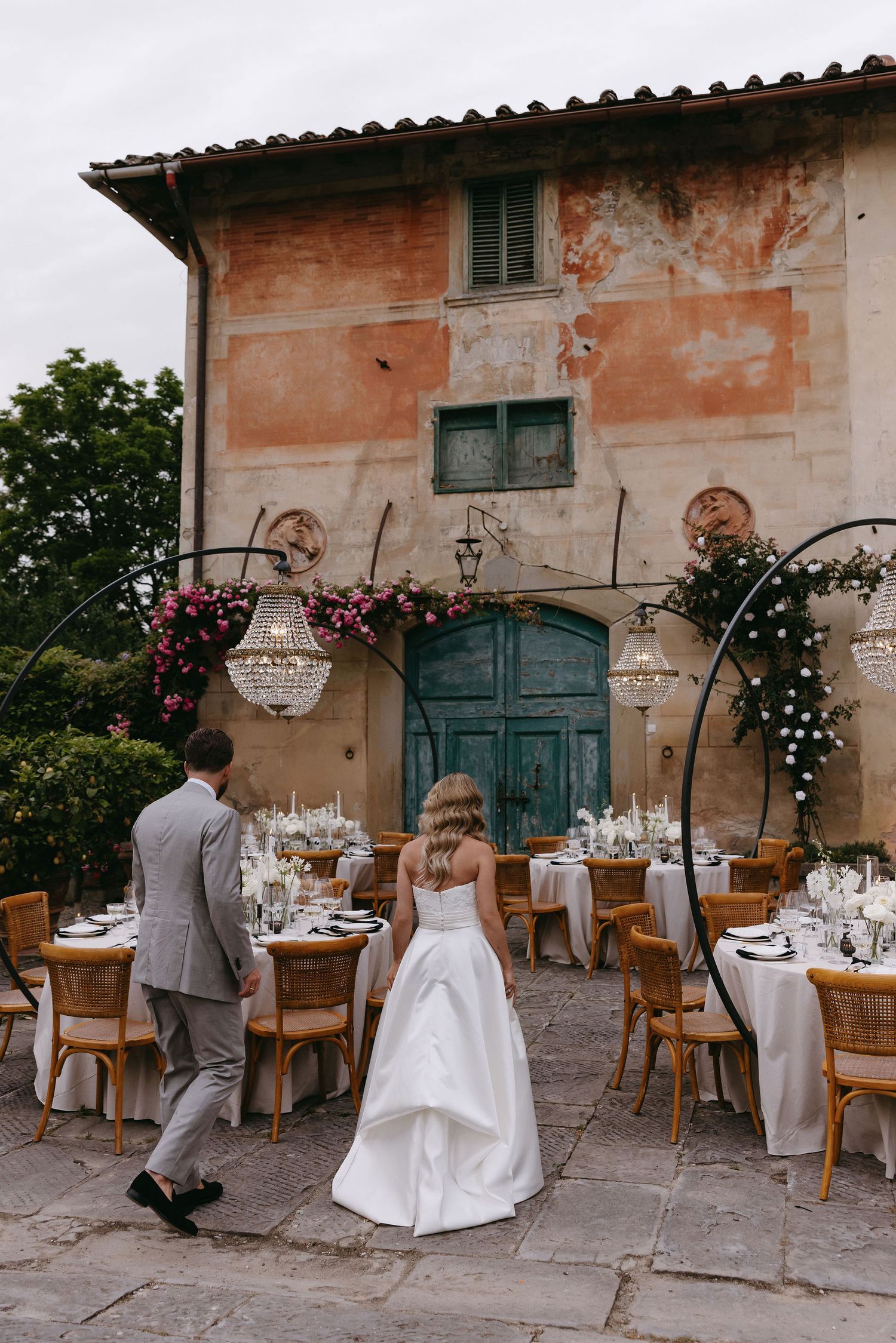 A romantic wedding reception setup outside an Italian villa with crystal chandeliers and flower arrangements.