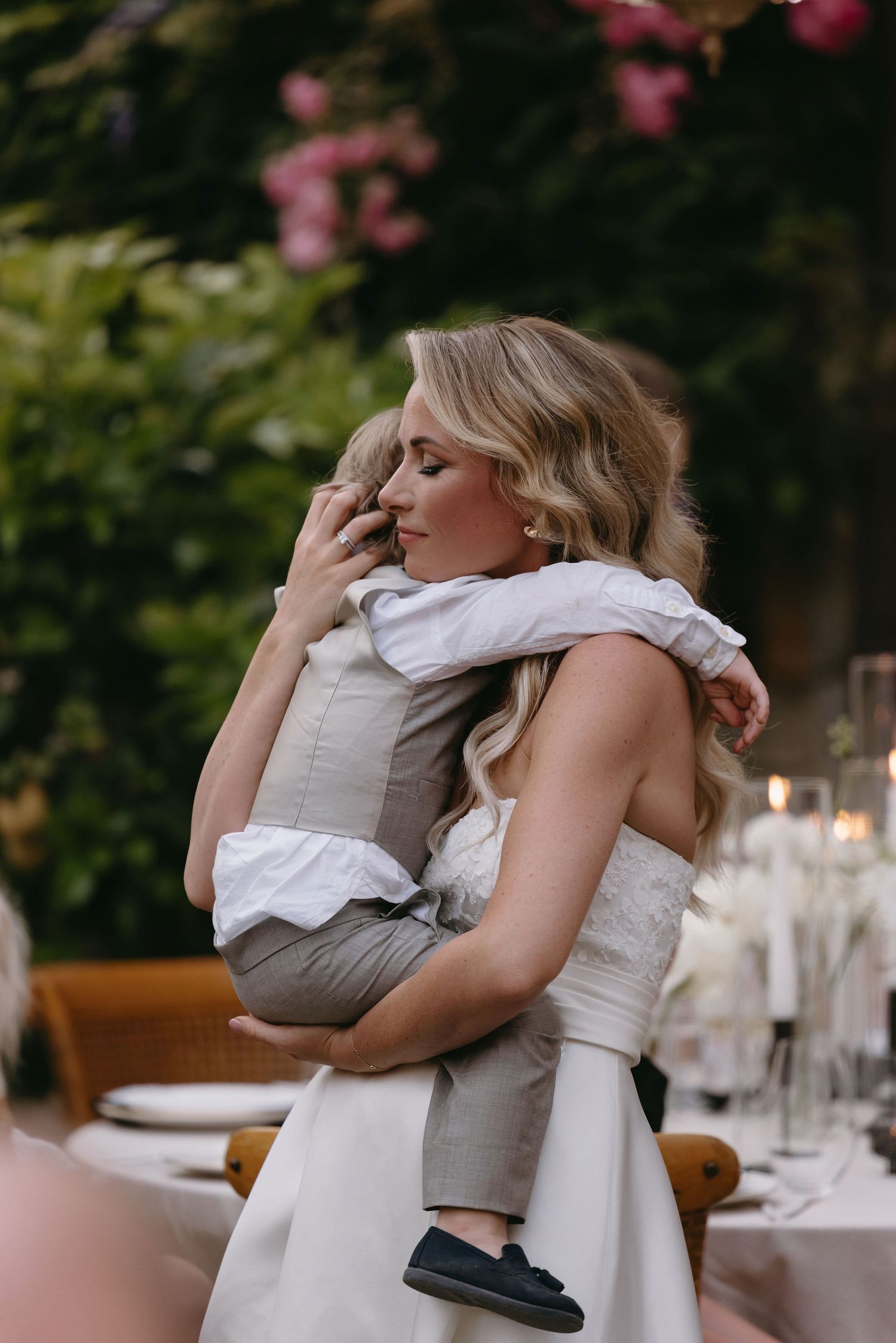 A tender moment at a wedding reception as a bride shares a dance with a young child outdoors.