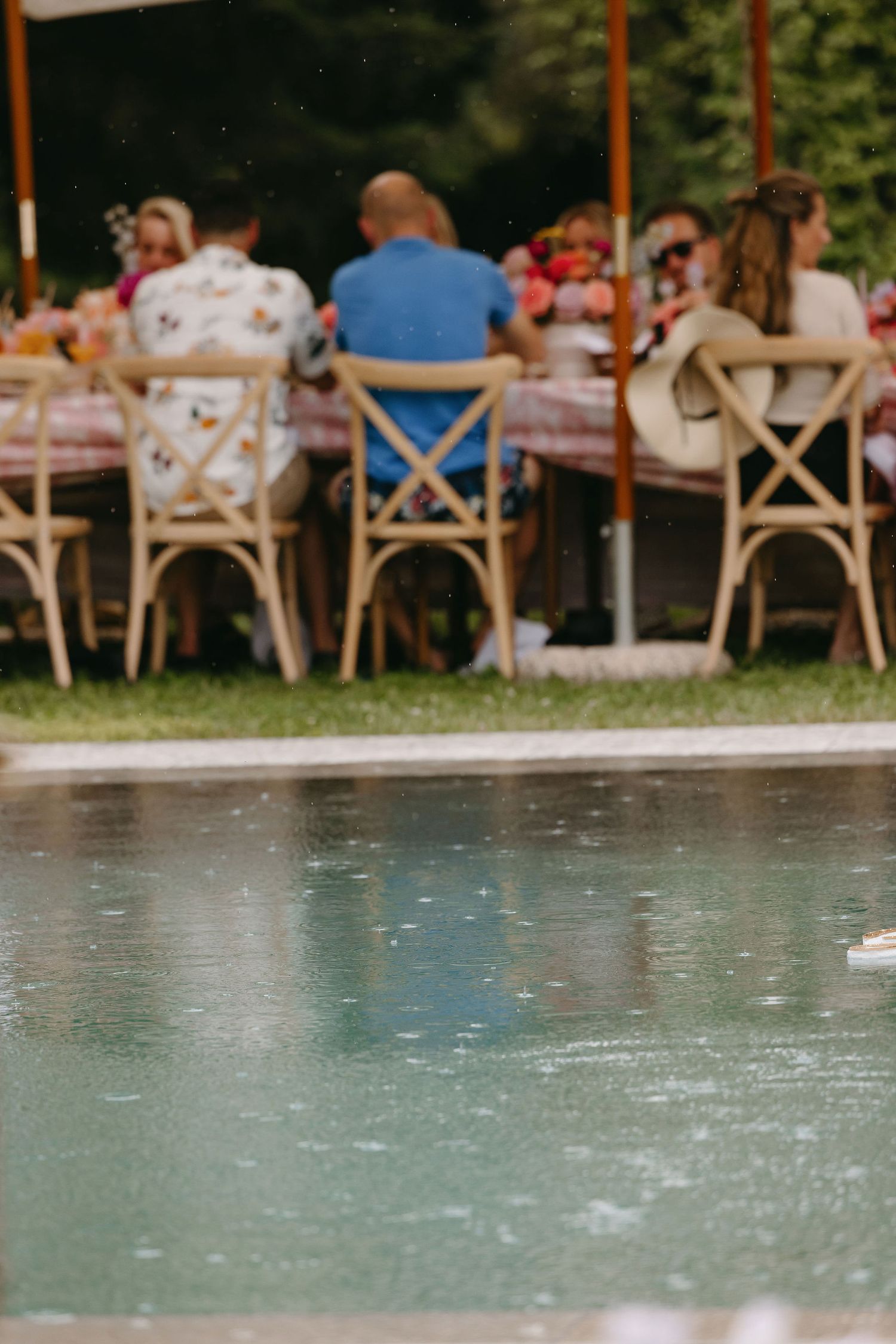 Guests dining at outdoor tables beside a swimming pool at an elegant event.