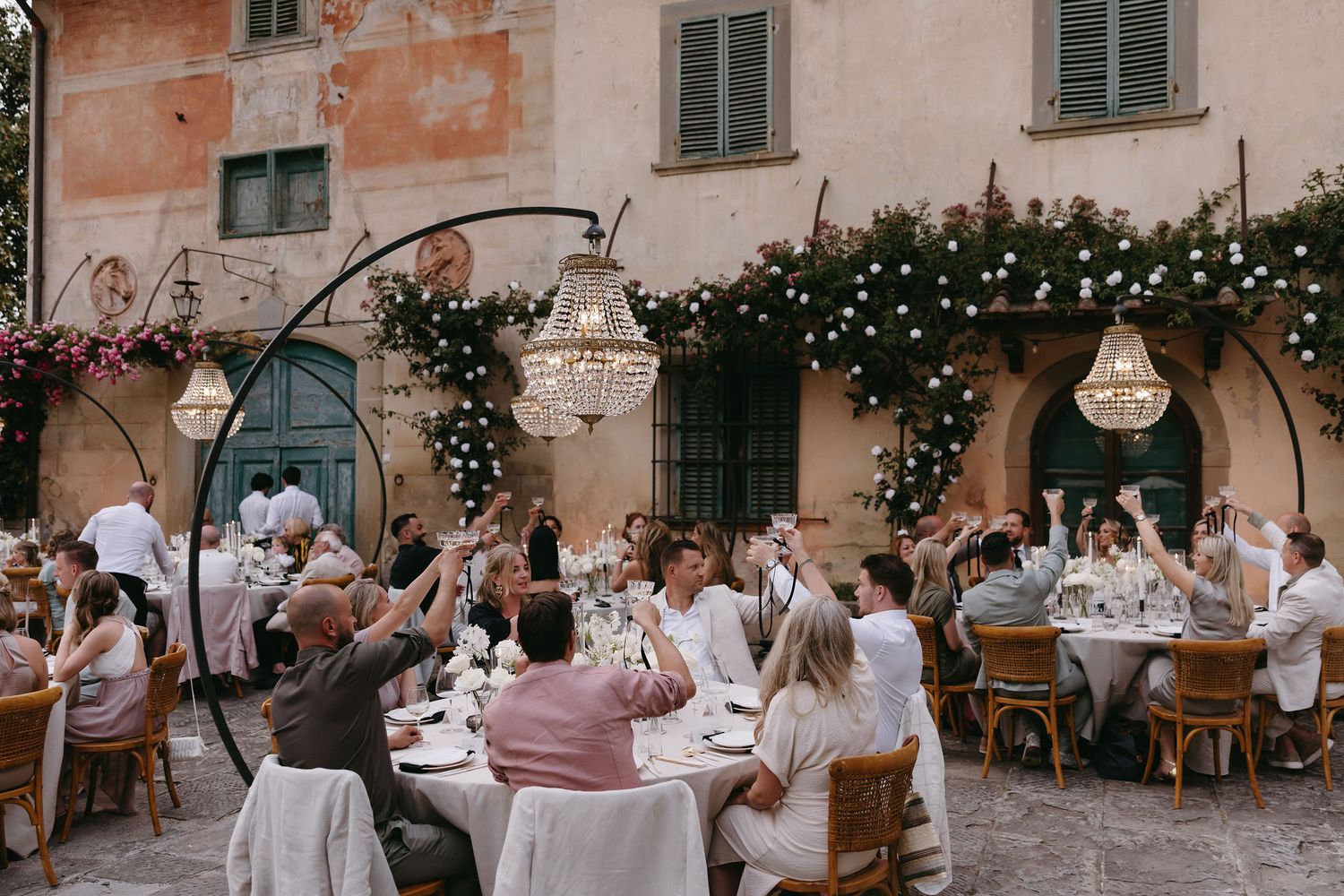 Outdoor Italian wedding reception with string lights and guests dining at long tables.