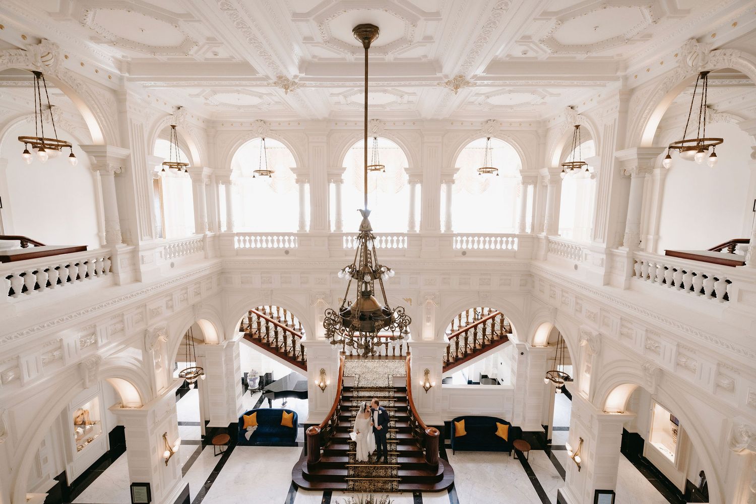 Elegant white ballroom interior with ornate chandeliers, curved staircases and classical architectural details.