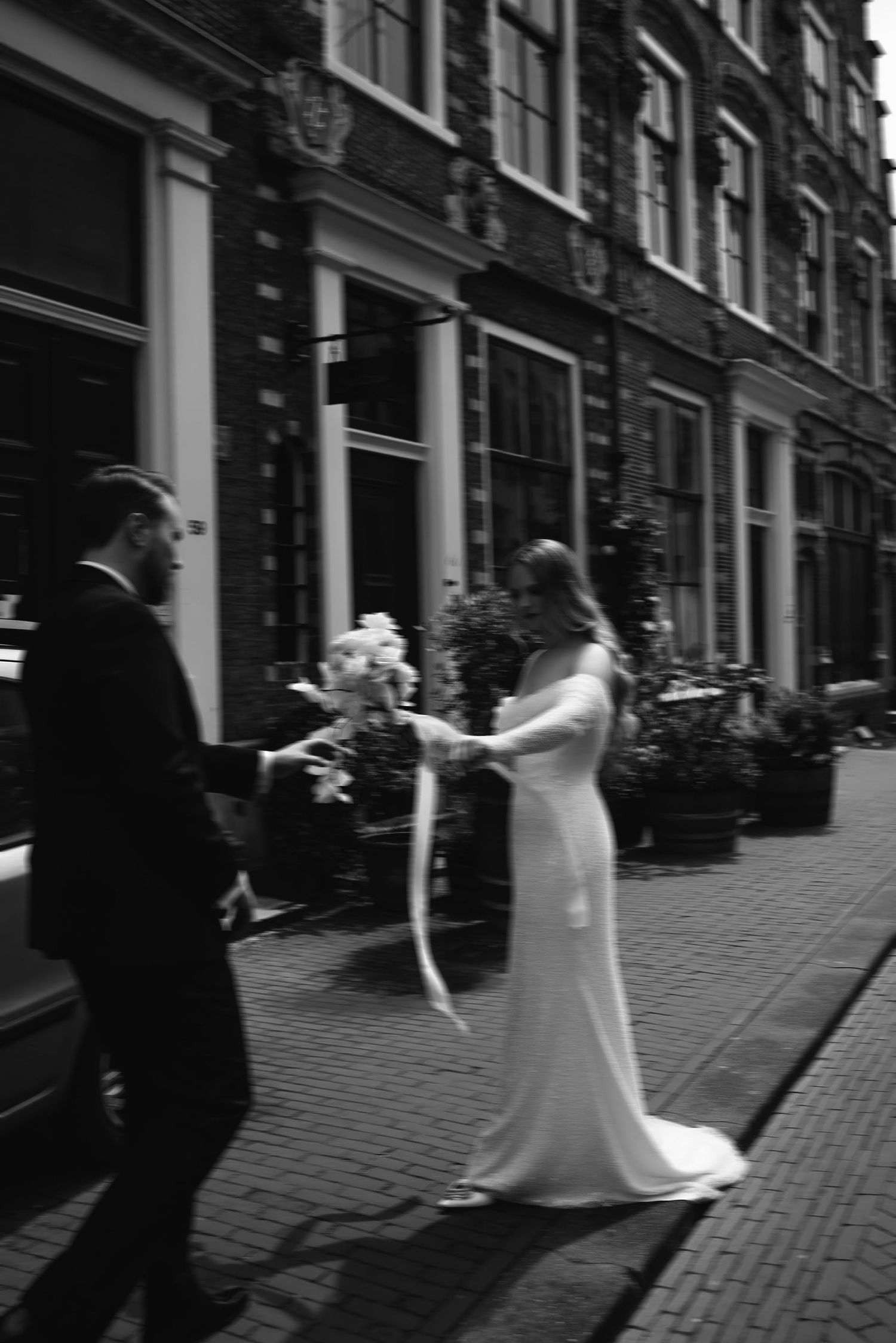 A black and white wedding sequence showing a couple playing and twirling on a cobblestone street in front of a building.