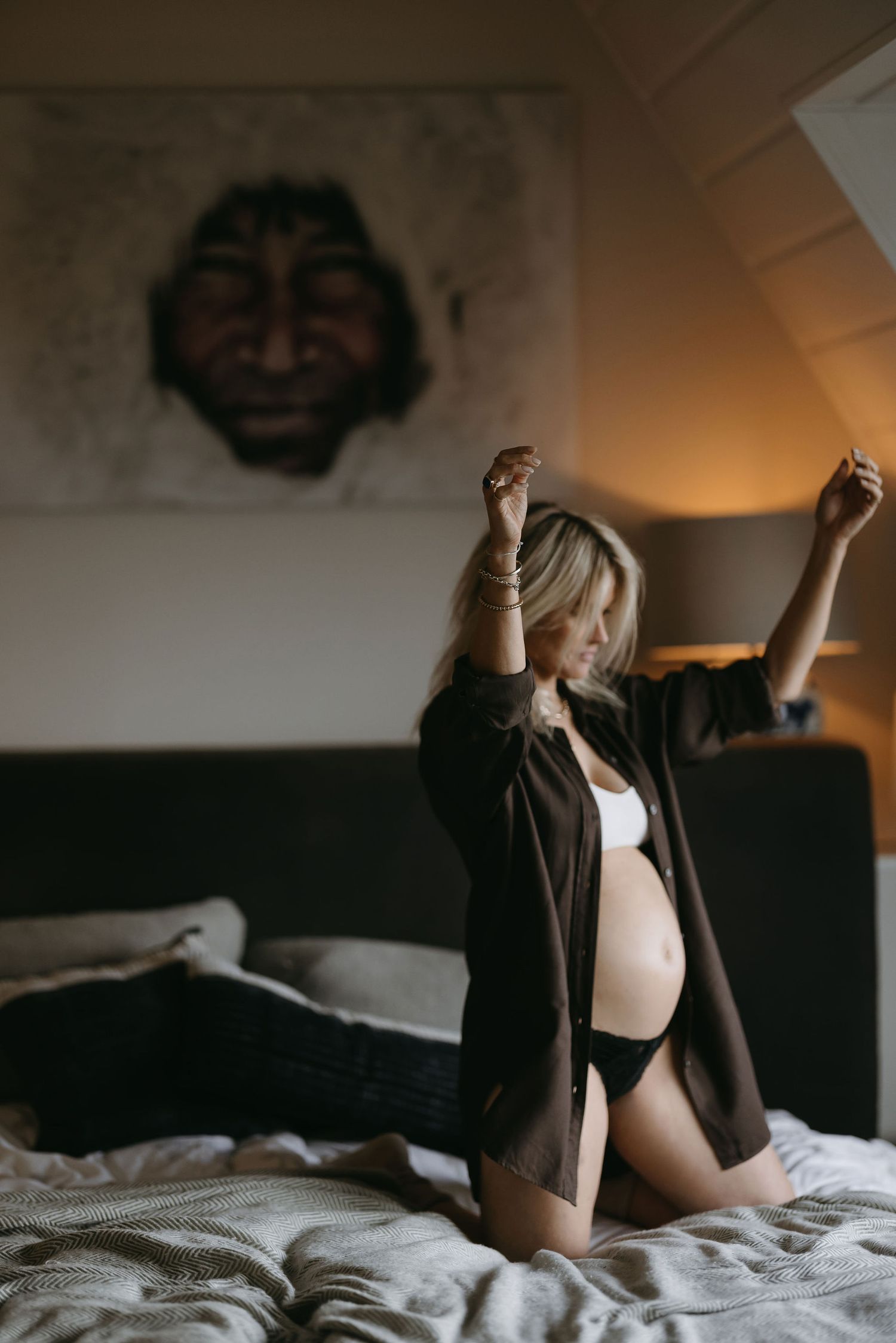 Artistic maternity boudoir photography with brown cardigan on white bedding.
