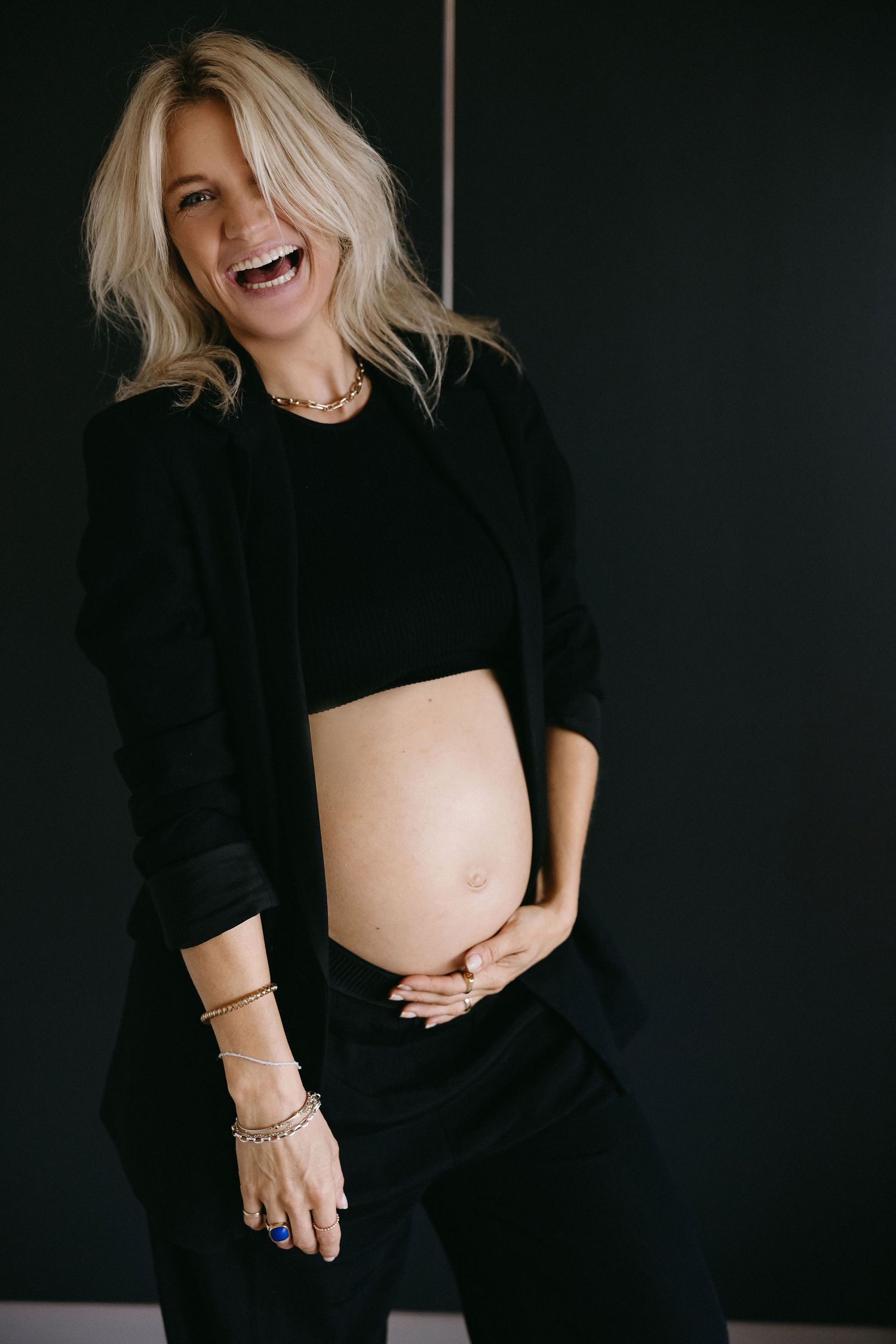 Maternity photo showing a joyful candid moment in a black outfit against dark background.