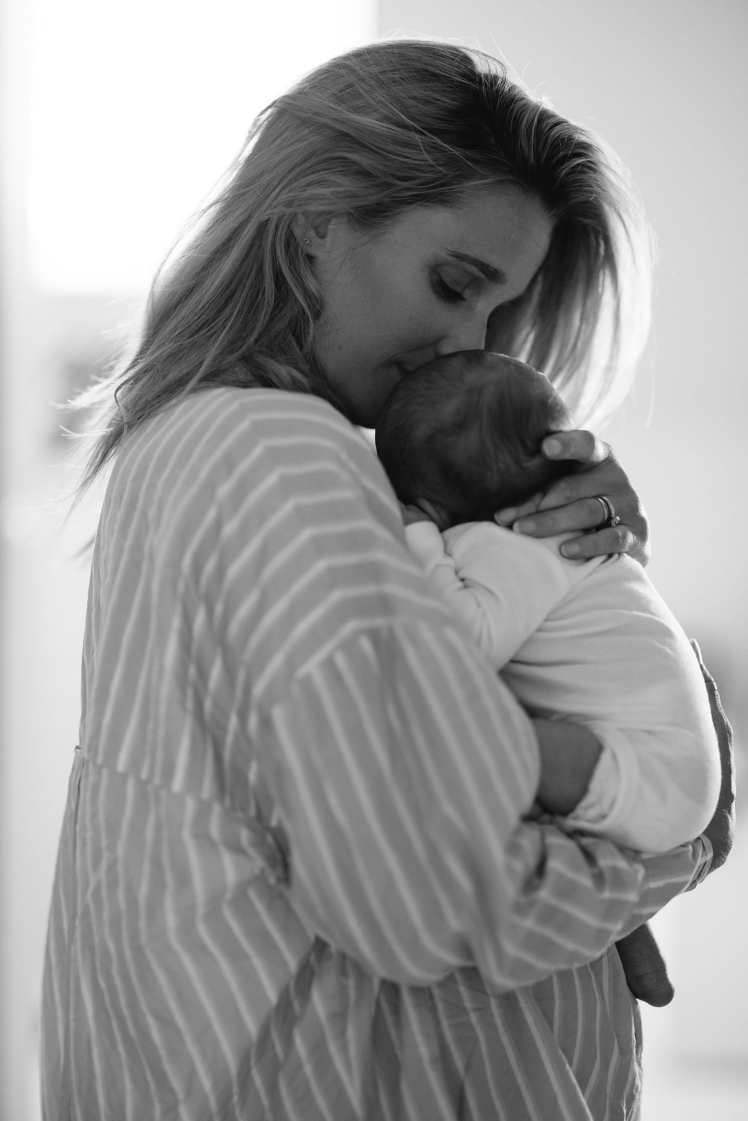 Black and white portrait of gentle embrace with newborn in striped shirt.