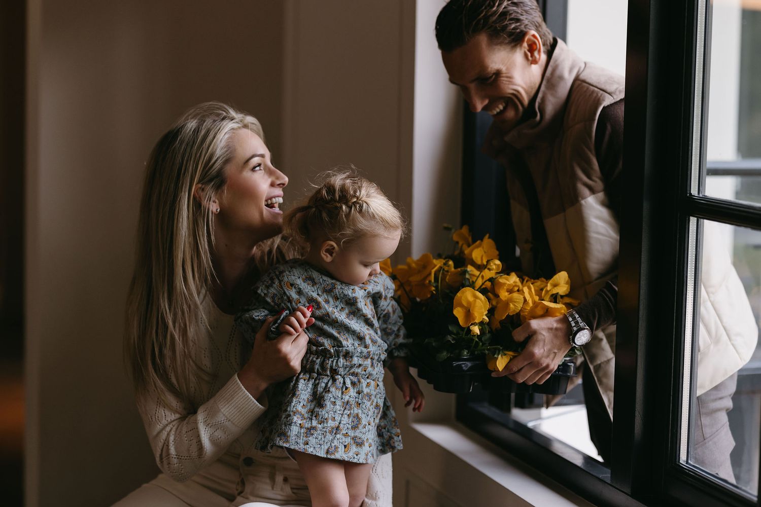 Intimate family moment by window with yellow sunflowers and natural light.