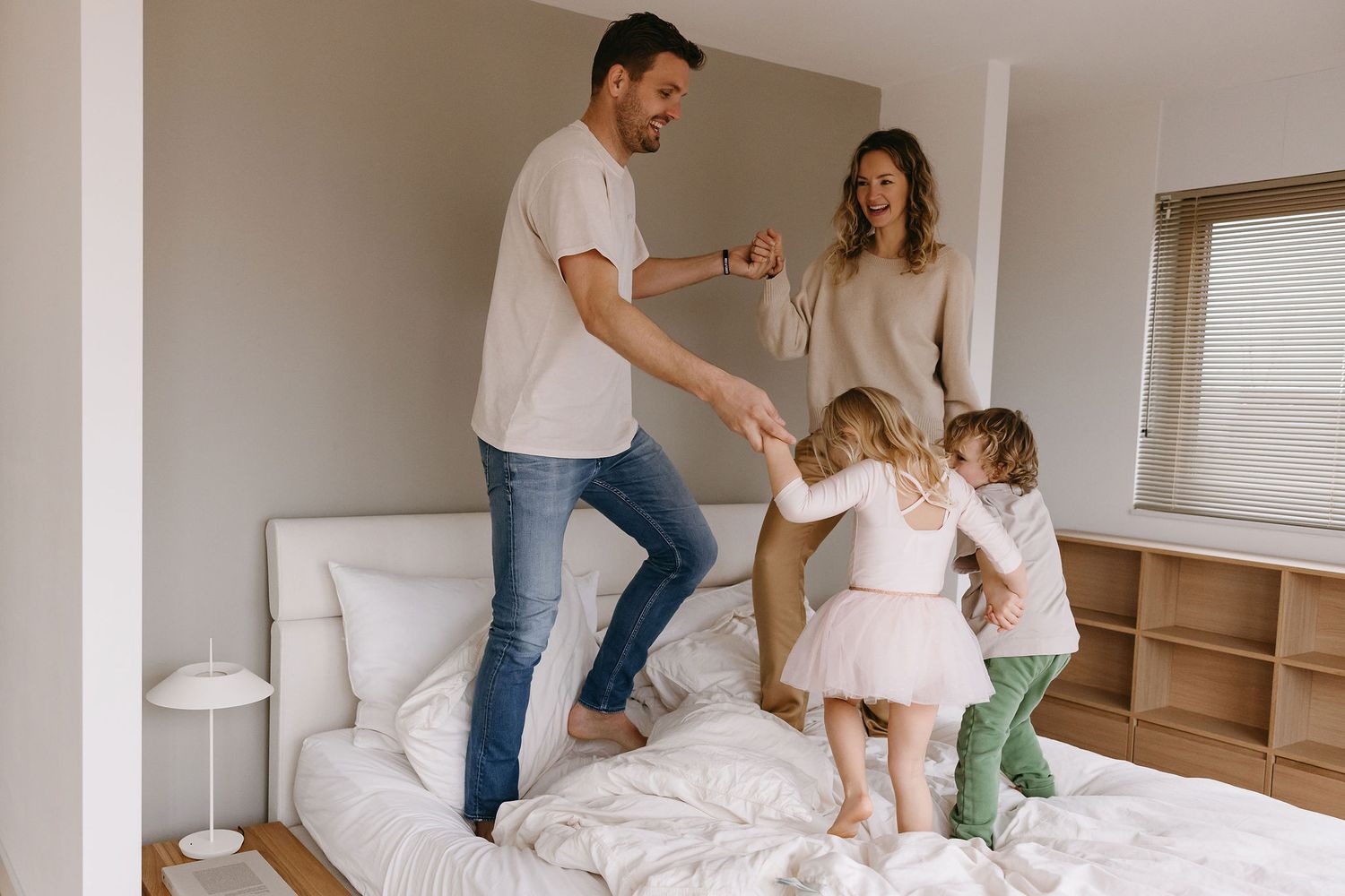 A family having fun jumping on the bed together in a bright, modern bedroom.