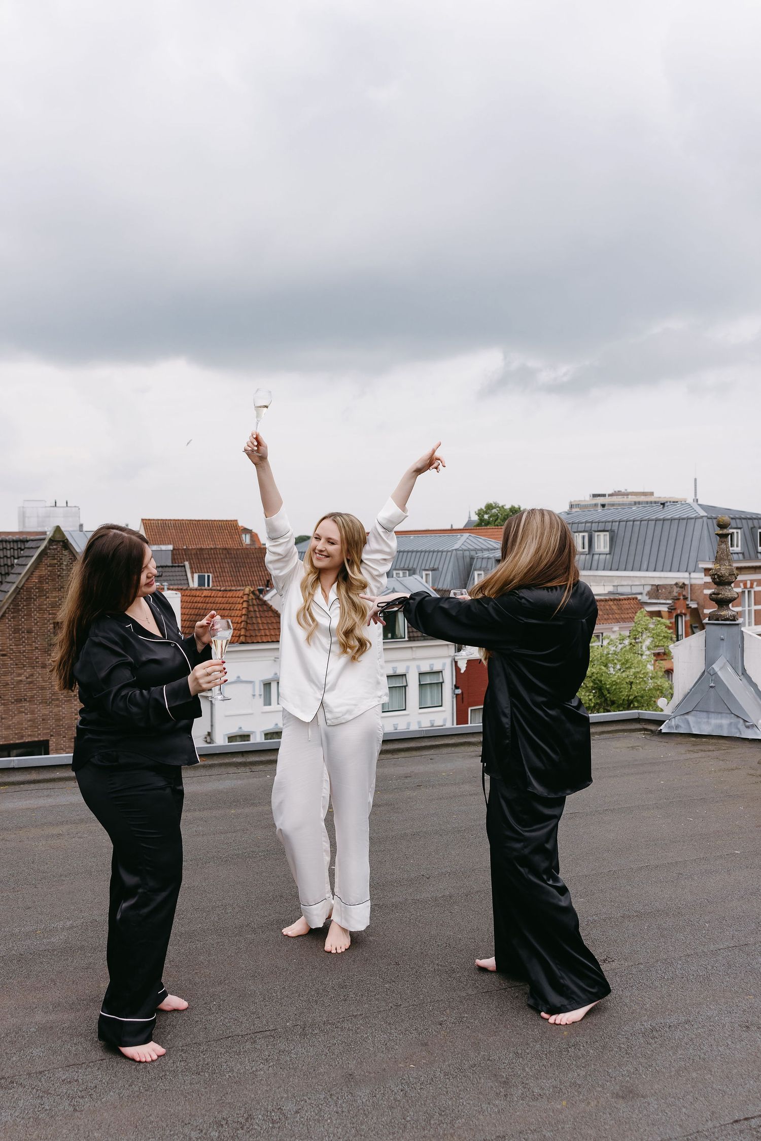 Three friends celebrate on rooftop in matching white and black outfits.