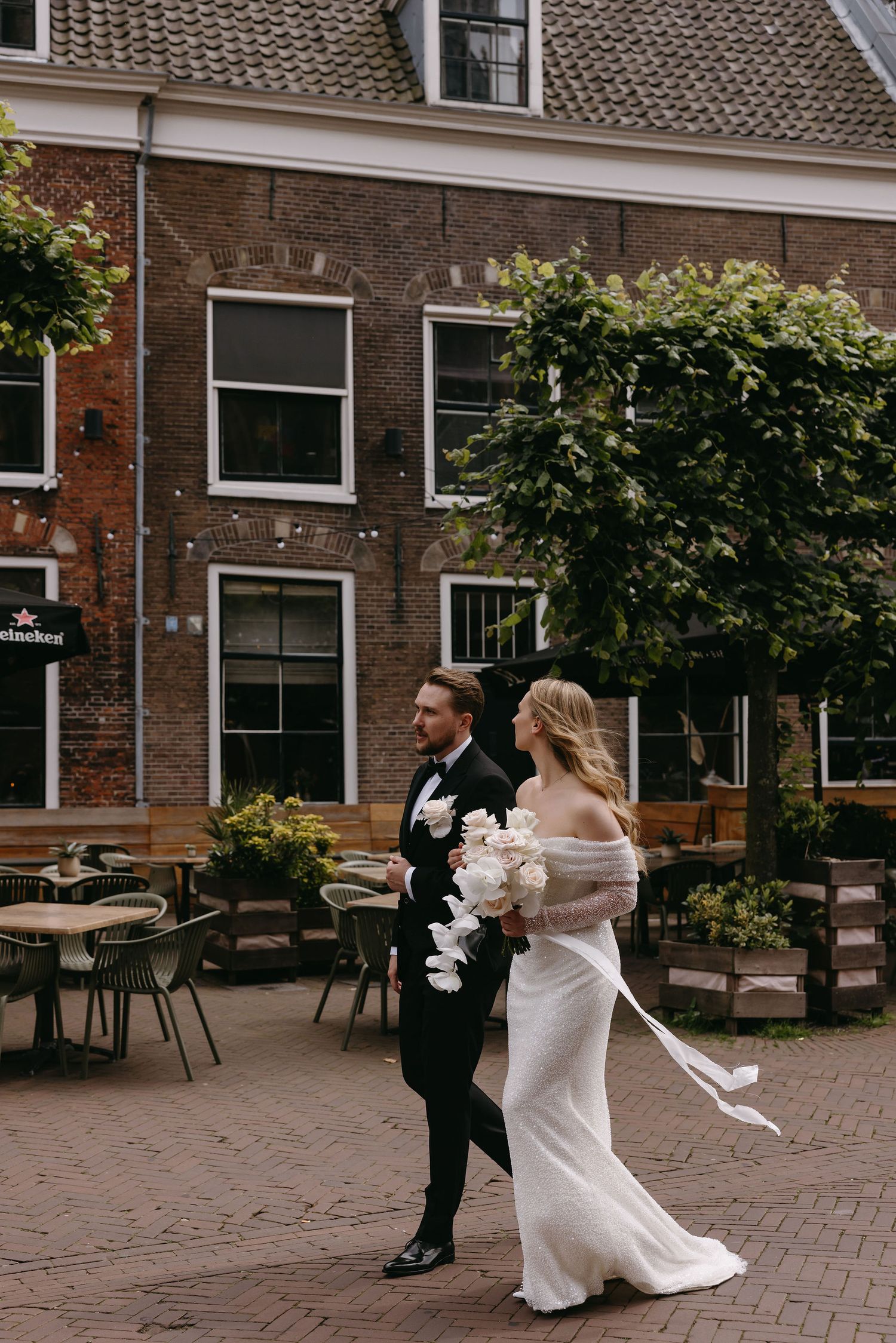 A couple walking together outside a historic brick building with outdoor cafe seating.