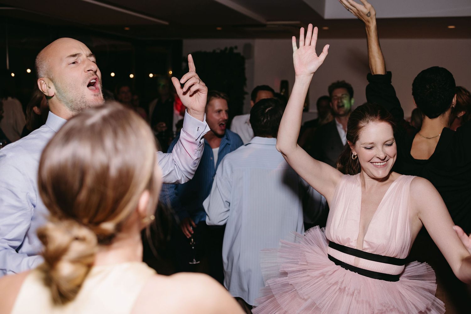 Energetic party guests dancing and celebrating at a dimly lit reception.