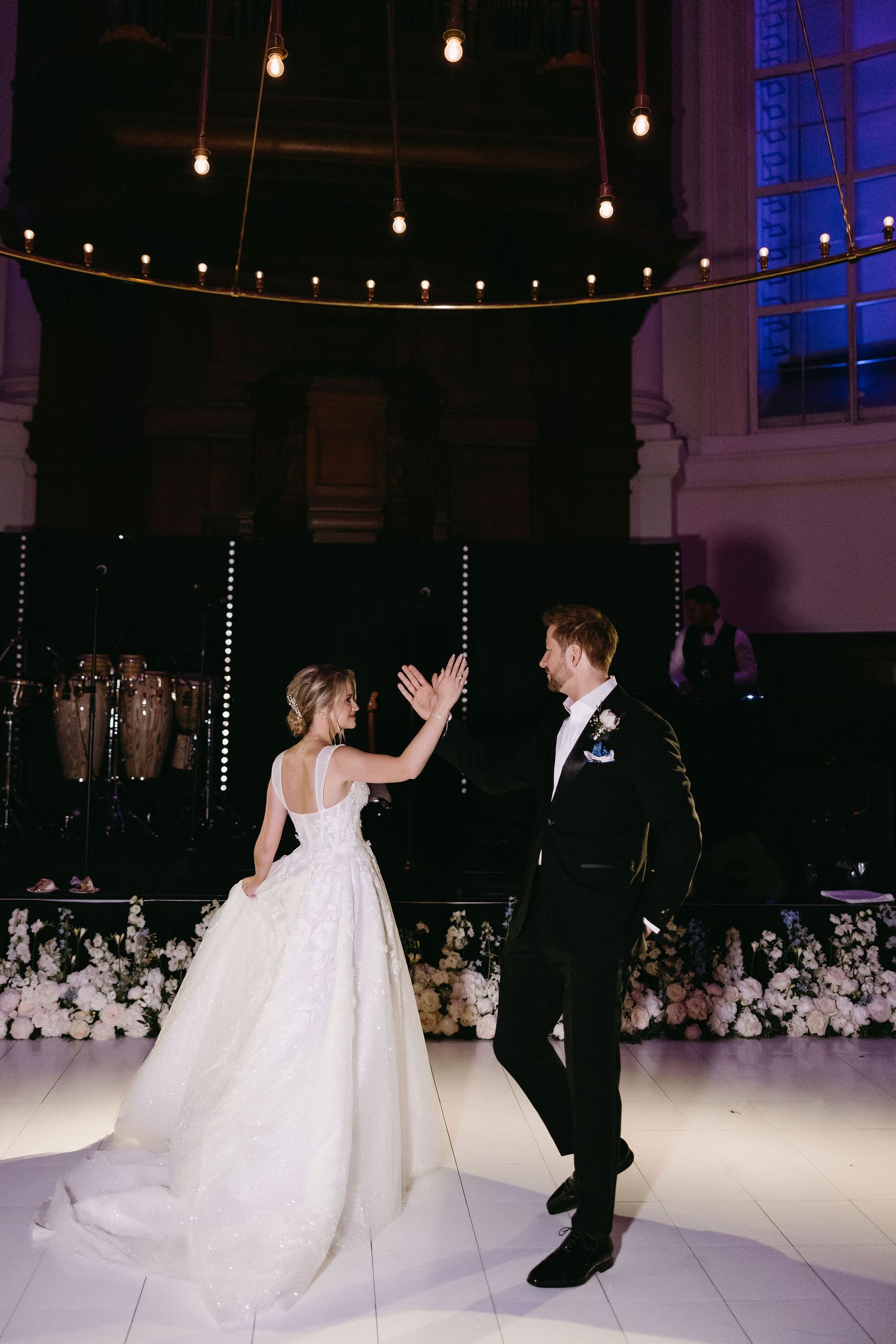 Couple sharing a celebratory dance moment under string lights at wedding reception.