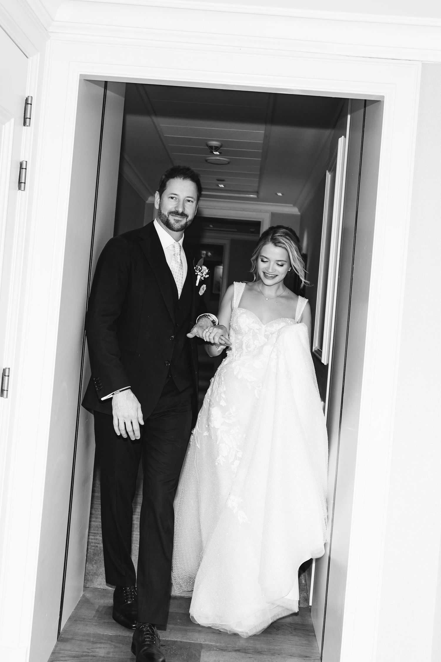 A couple walks together through a bright hallway on their wedding day.