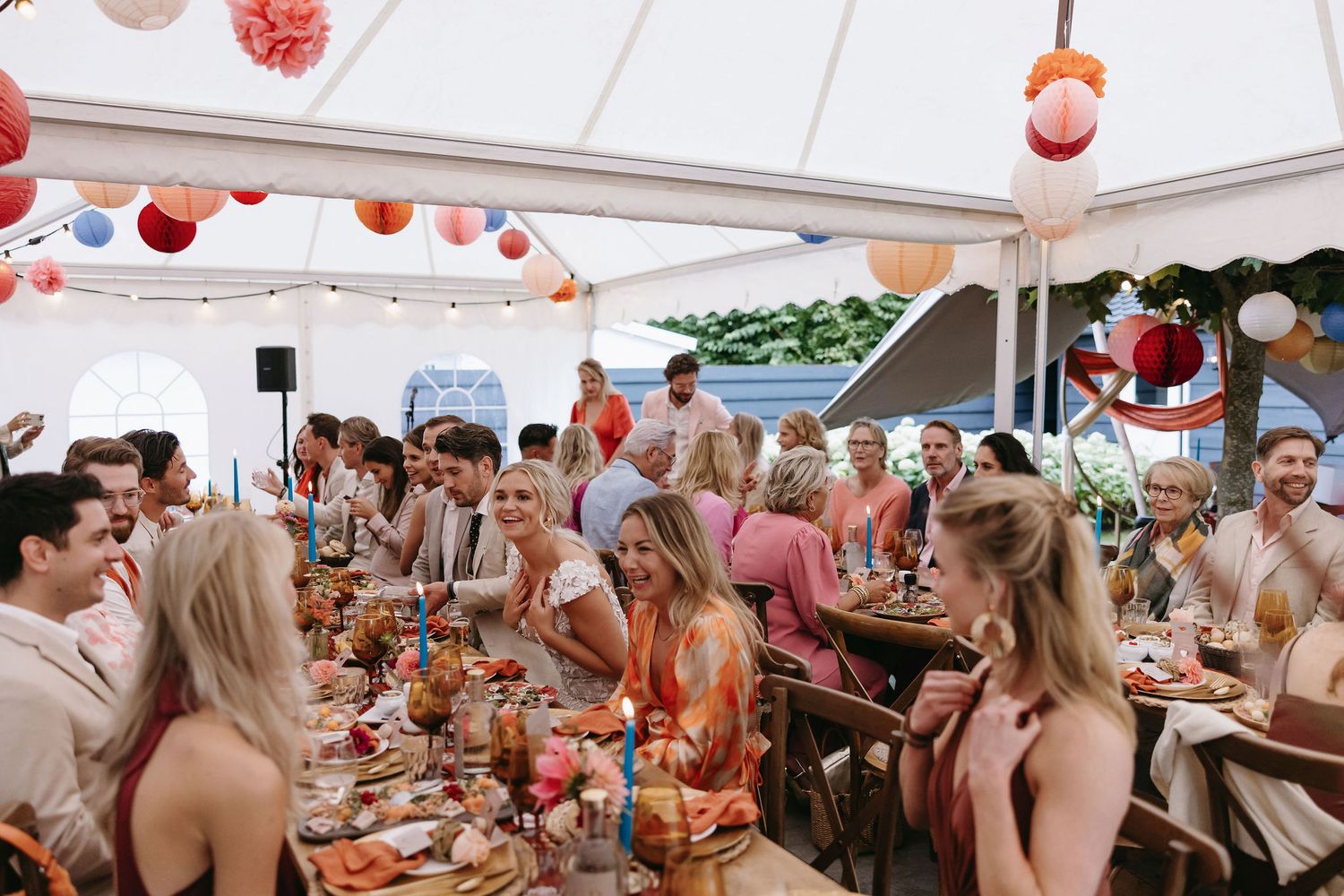 Outdoor wedding reception under white tent with coral and peach paper lantern decorations.