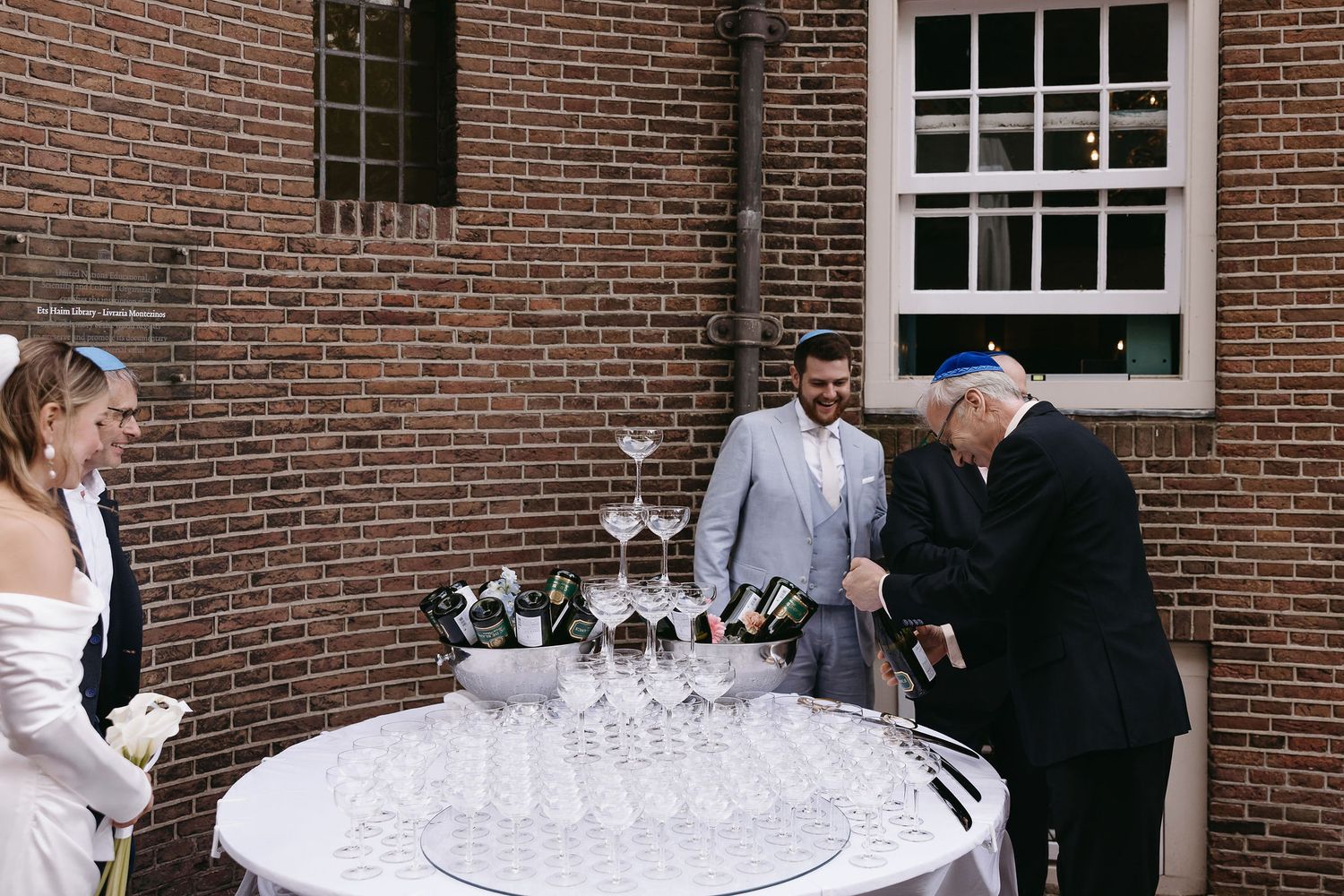 Wedding guests gather around a table with champagne glasses at a brick venue.