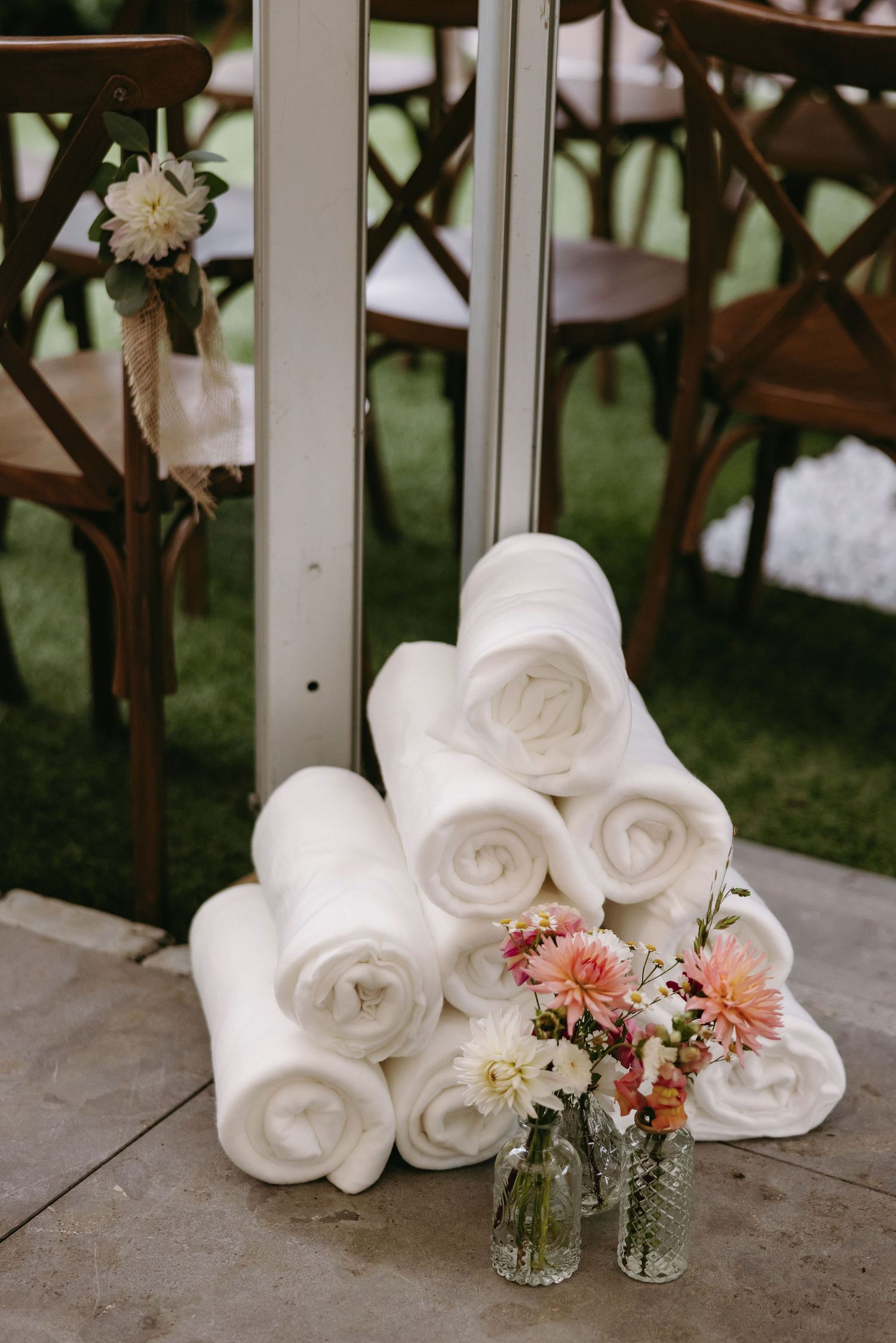 White rolled towels stacked beside delicate floral arrangement in glass vases.