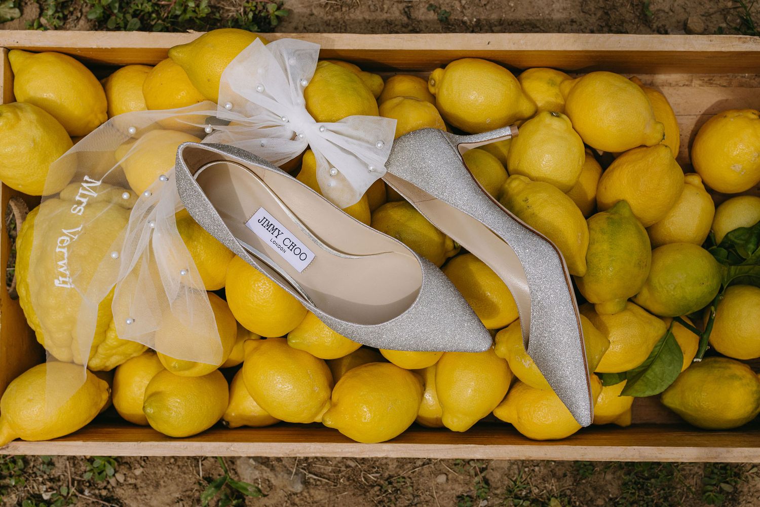 Elegant grey bridal shoes placed on a wooden crate filled with fresh yellow lemons.