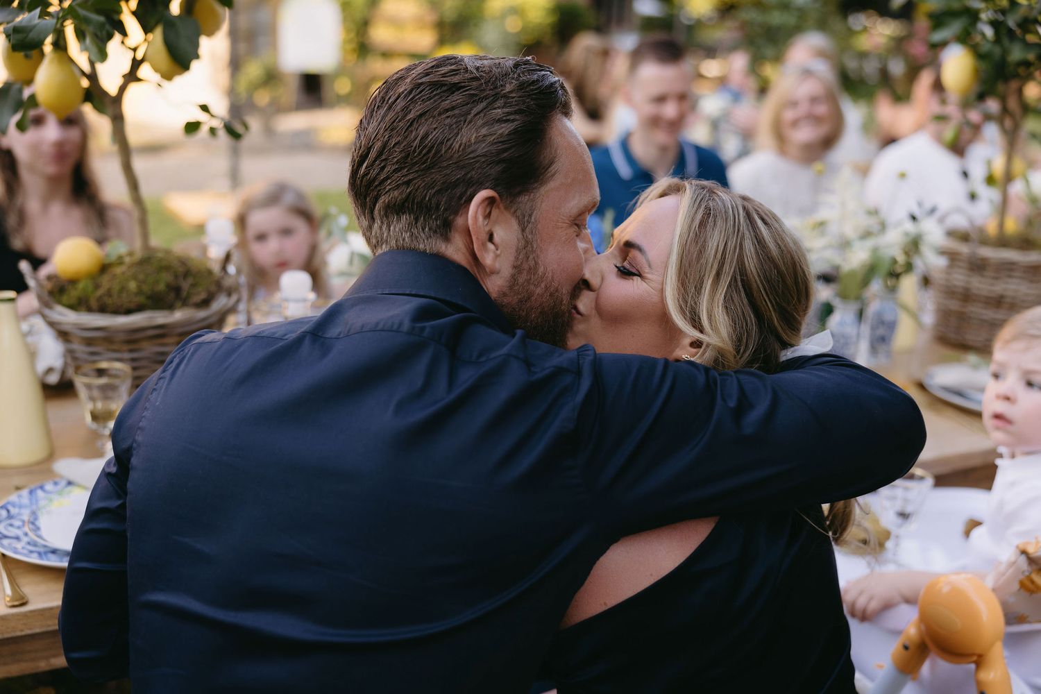A couple shares a romantic kiss during a wedding celebration in an outdoor garden setting.