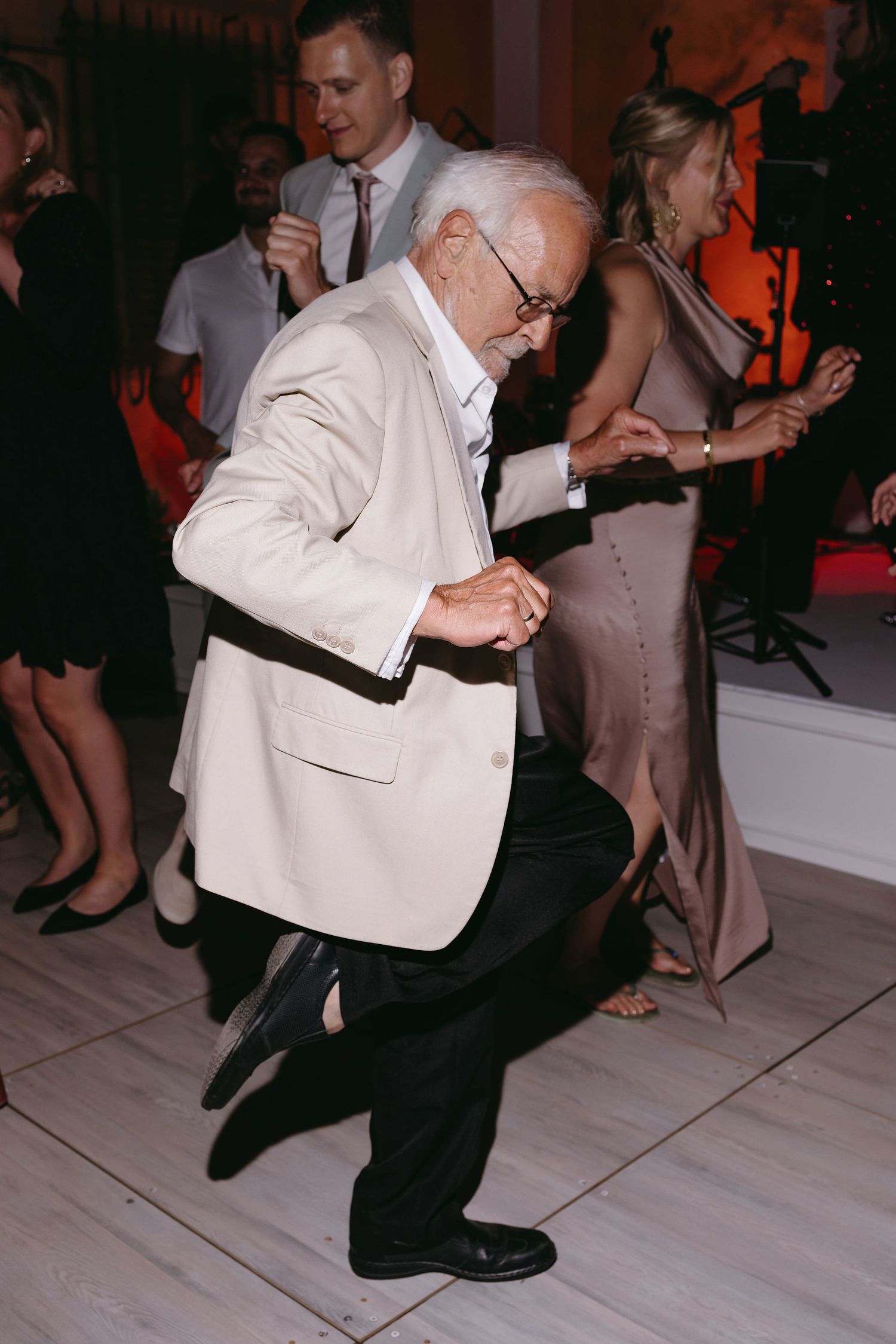 A gentleman in a white jacket dancing energetically on a light-colored dance floor.