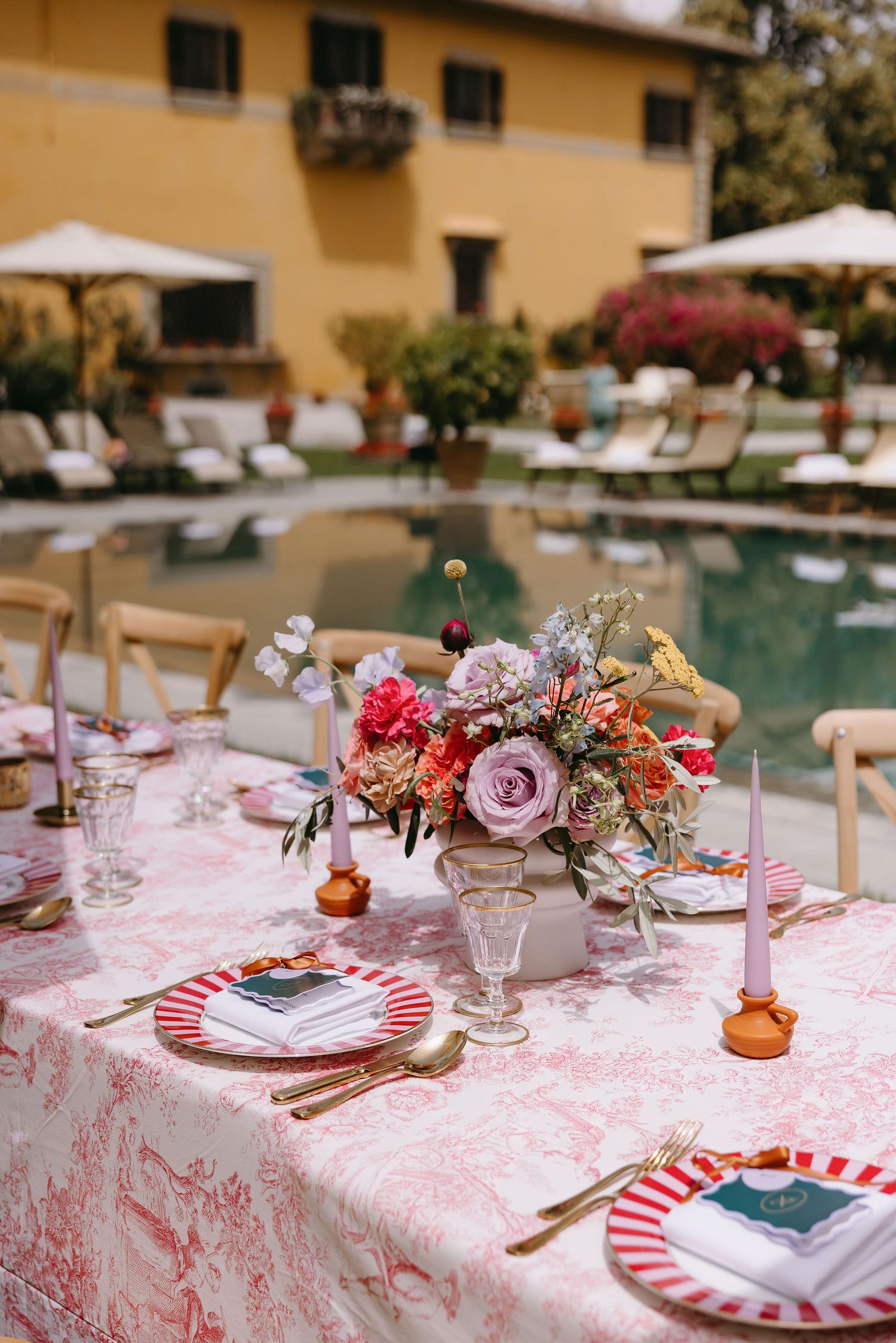 Romantic table setting with pink floral centerpiece and striped plates by a pool.