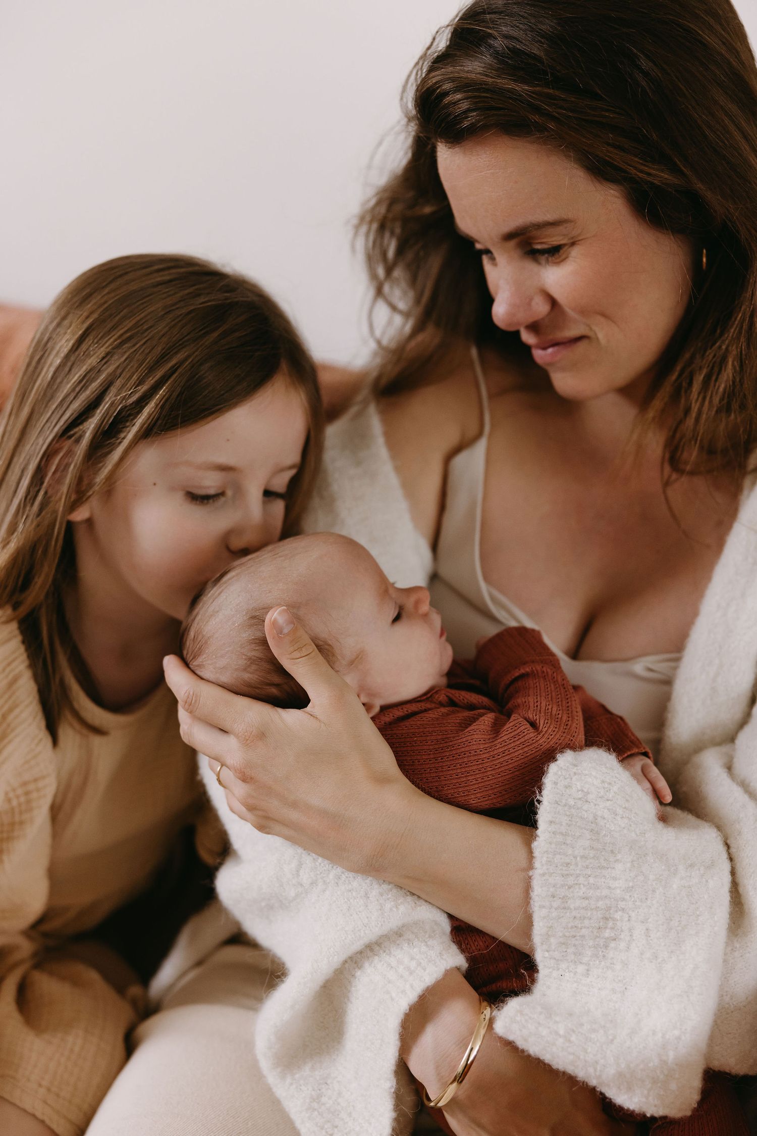A tender family moment as they gaze lovingly at a newborn baby wrapped in burgundy clothing.