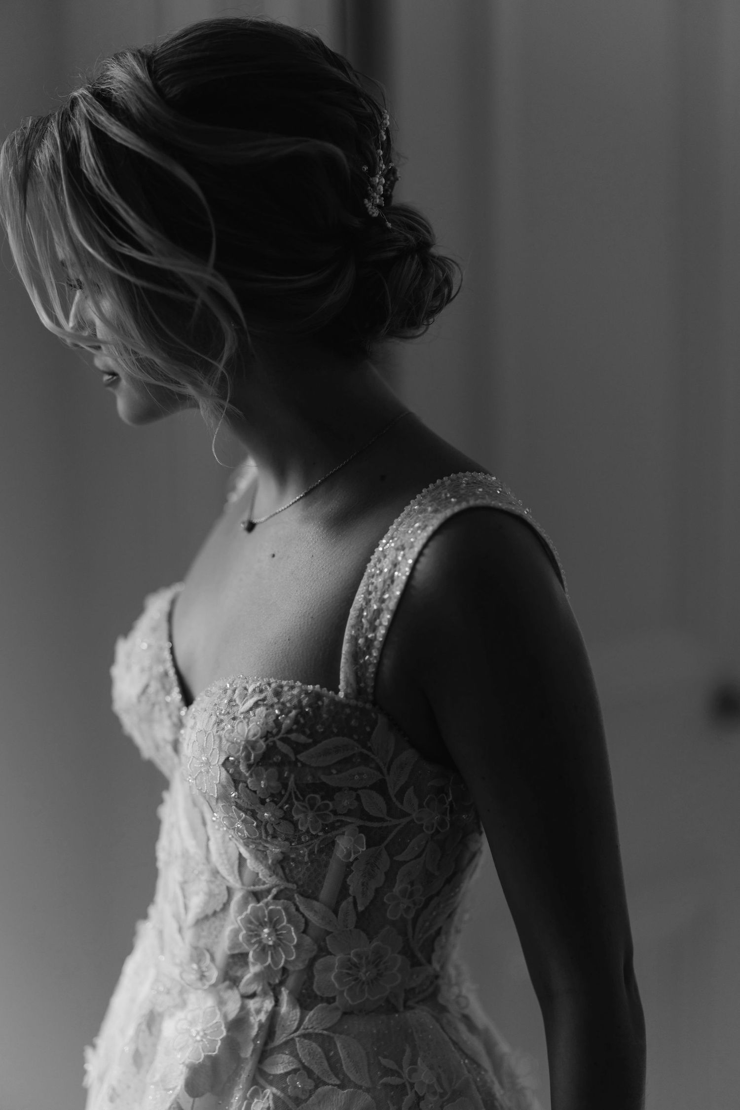 Artistic monochrome image capturing the intricate lace details of a bridal gown in dramatic side lighting.
