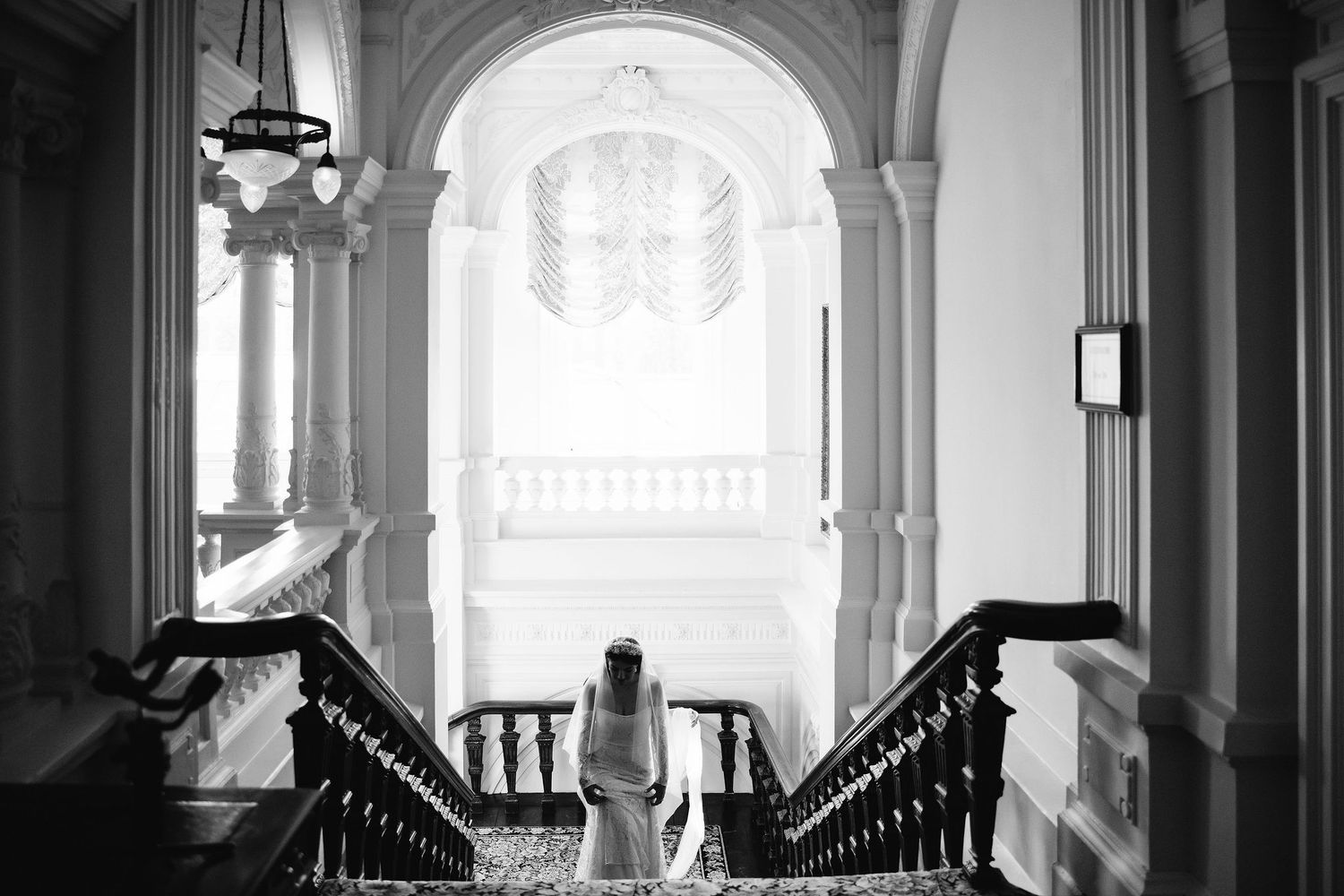 Black and white view of a grand staircase in a historic building with ornate architectural details and arched window.