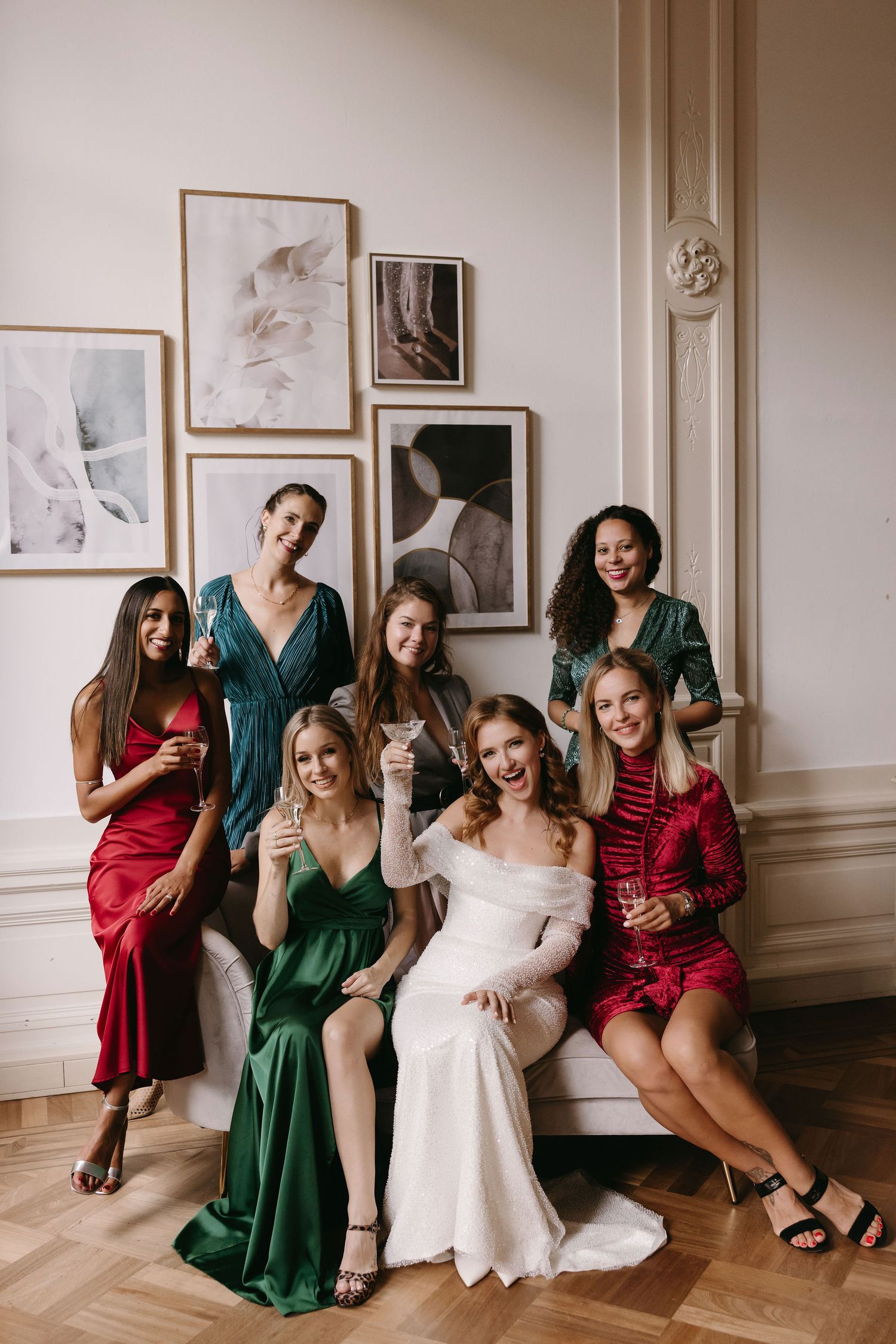 Bridal party in red and green dresses posing together in an elegantly decorated room.