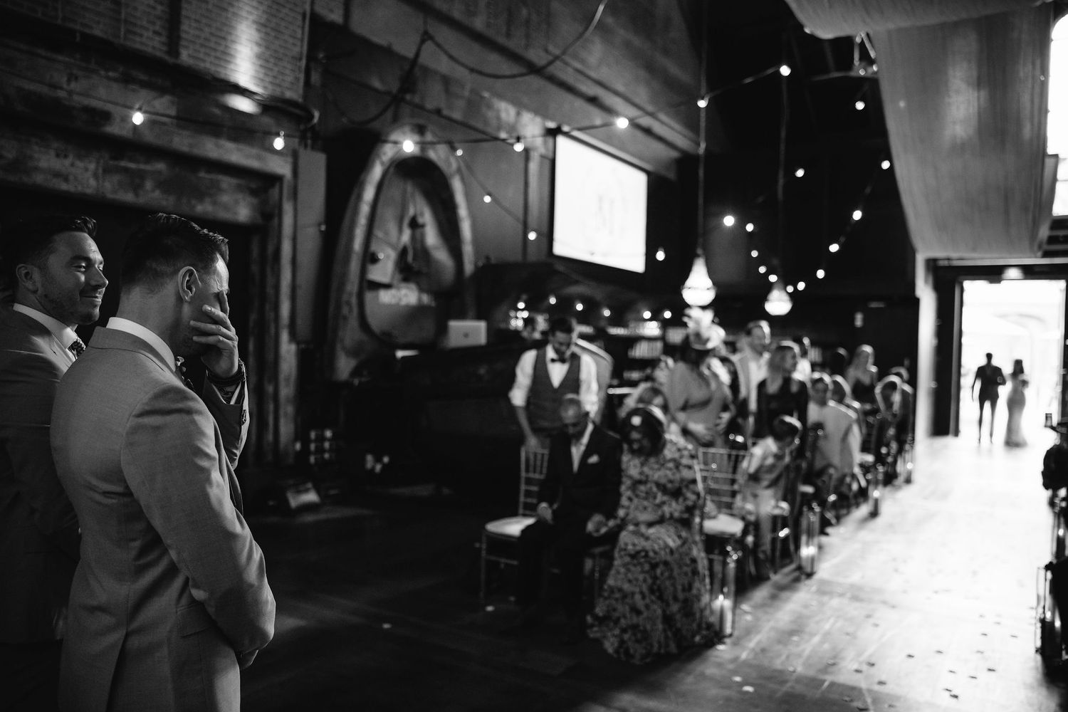 Black and white photo of wedding guests lining a venue hallway with string lights.