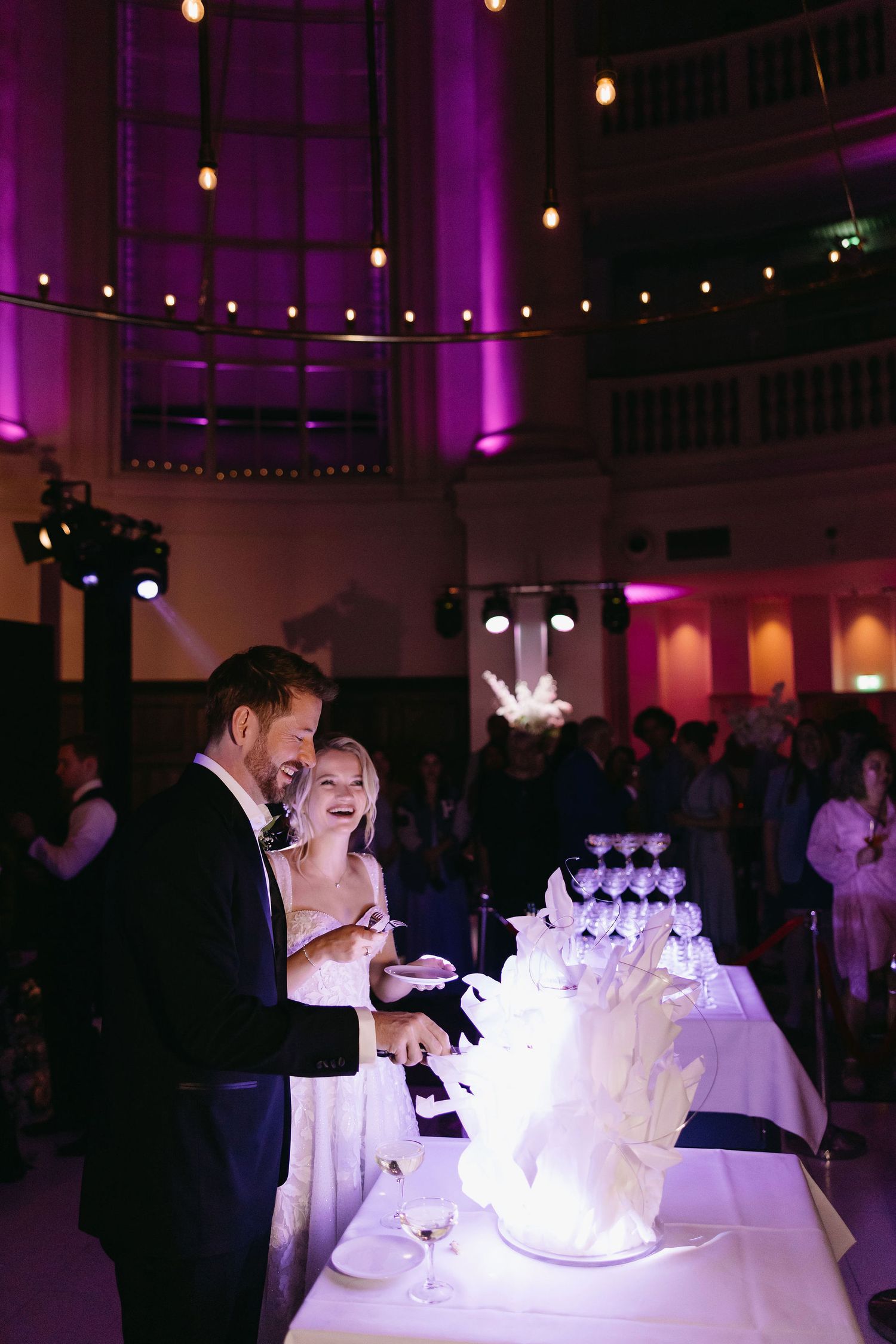 Wedding reception venue with dramatic purple lighting and illuminated multi-tiered cake display.