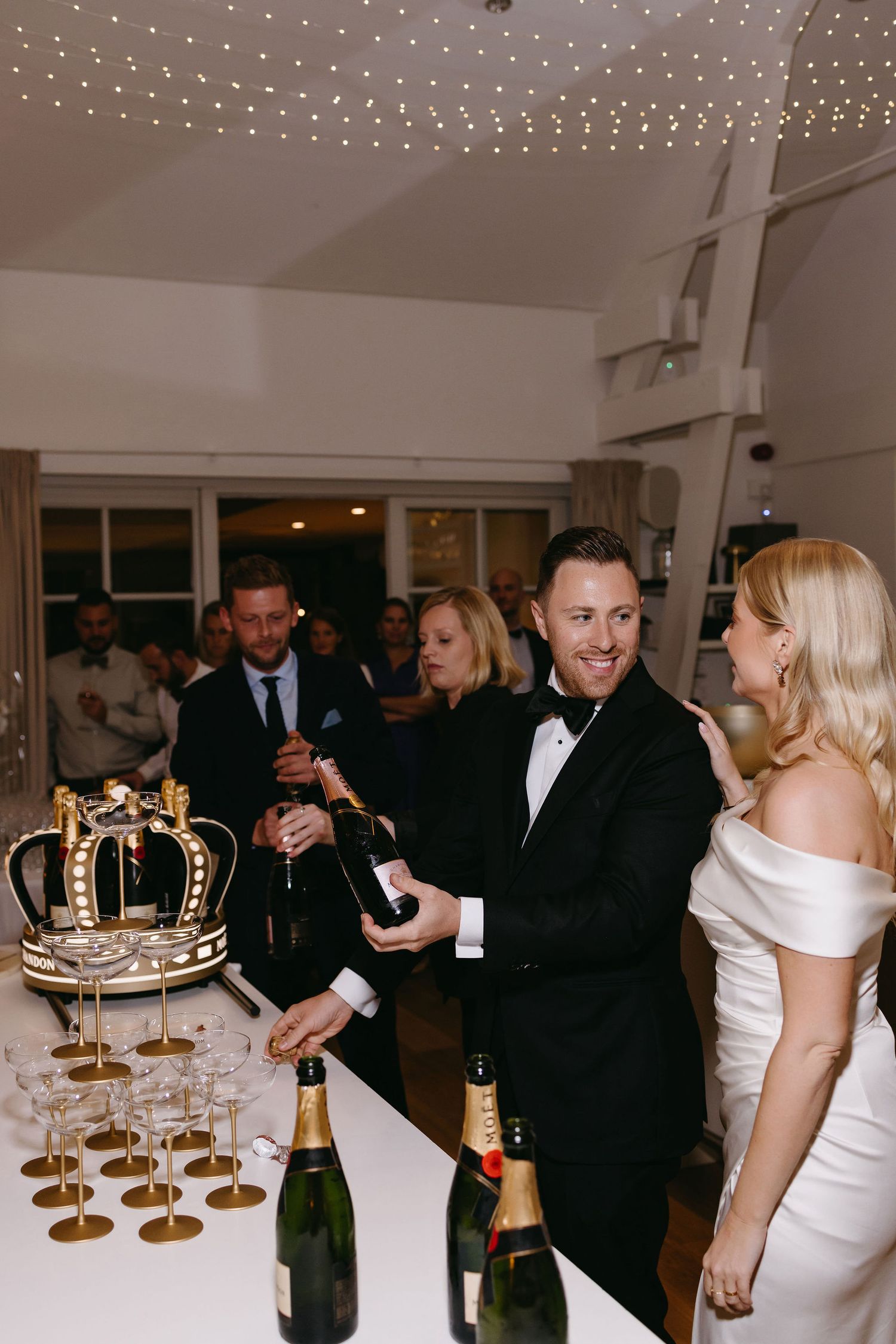 Wedding reception with champagne tower and decorative crown display while guests celebrate.