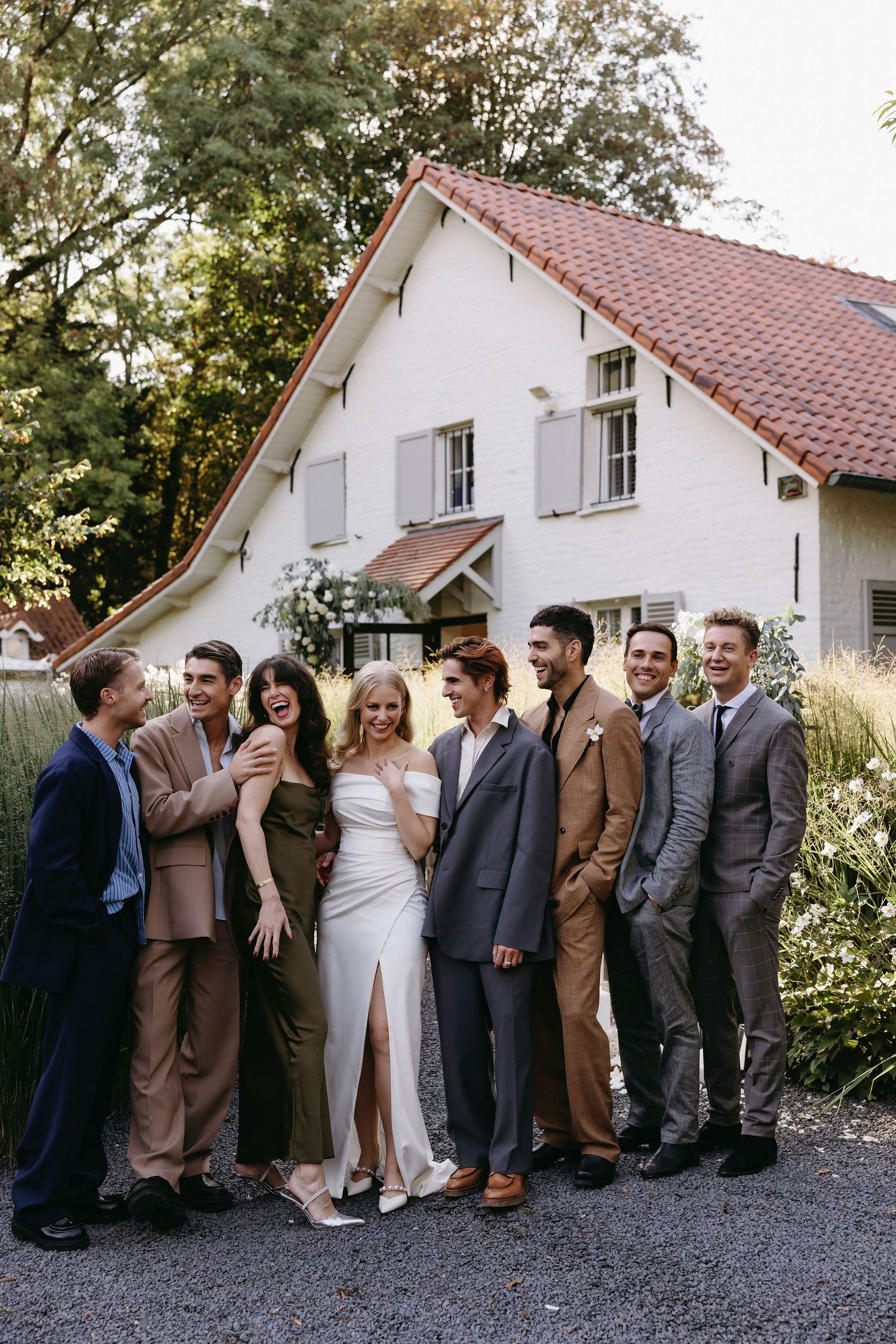 Wedding party lined up against a white house exterior for fun group photos.