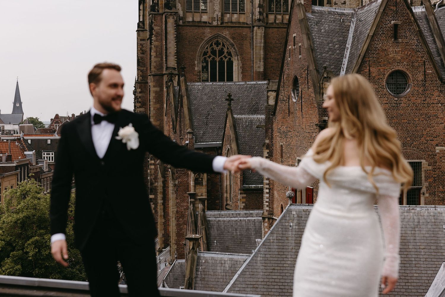 Couple in wedding attire sharing a moment on a church rooftop with gothic architecture in background.