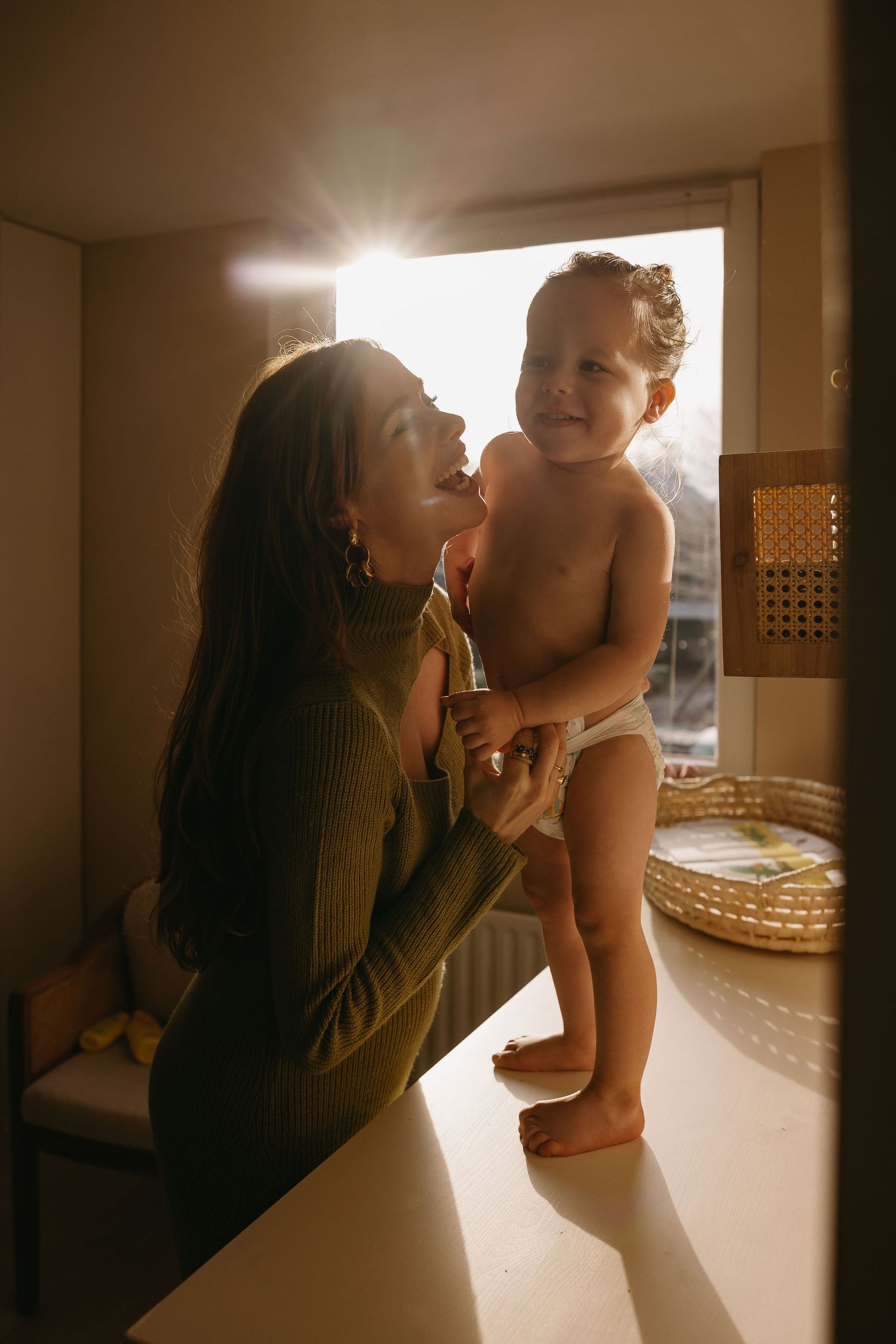 A tender parenting moment captured in warm backlit tones showing playful interaction in a cozy interior setting.